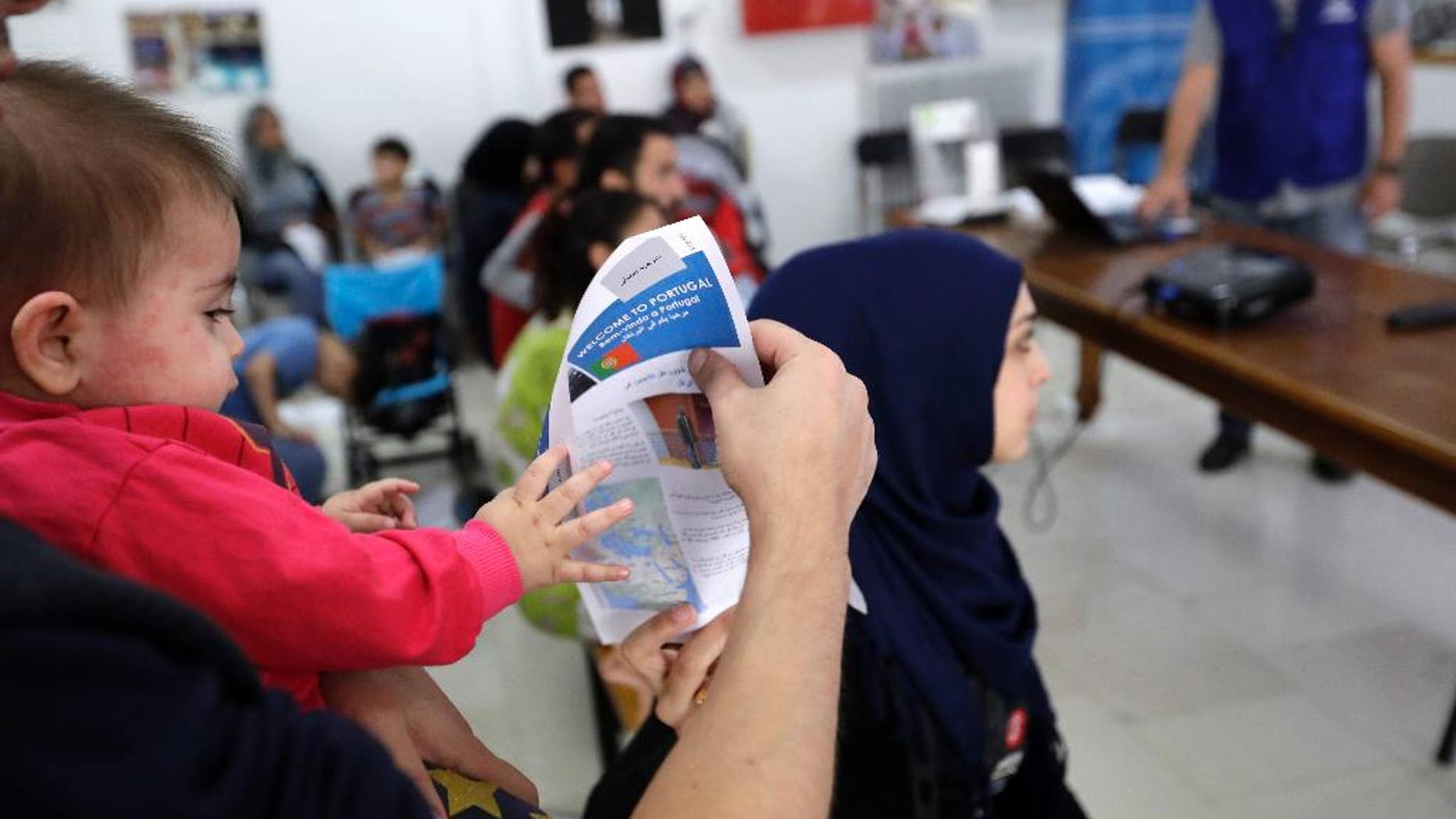 A child tries to takes a flyer from his father's hand as a group of 27 refugees takes part in an orientation program at International Organization of Migration office in Athens, Tuesday, Sept. 27, 2016, one day before being relocated to Portugal. The program should have seen 66,400 people from Greece relocated across the EU over two years from Sept. 16 last year, but to date just over 4,130 people have been resettled. (AP Photo/Thanassis Stavrakis)
