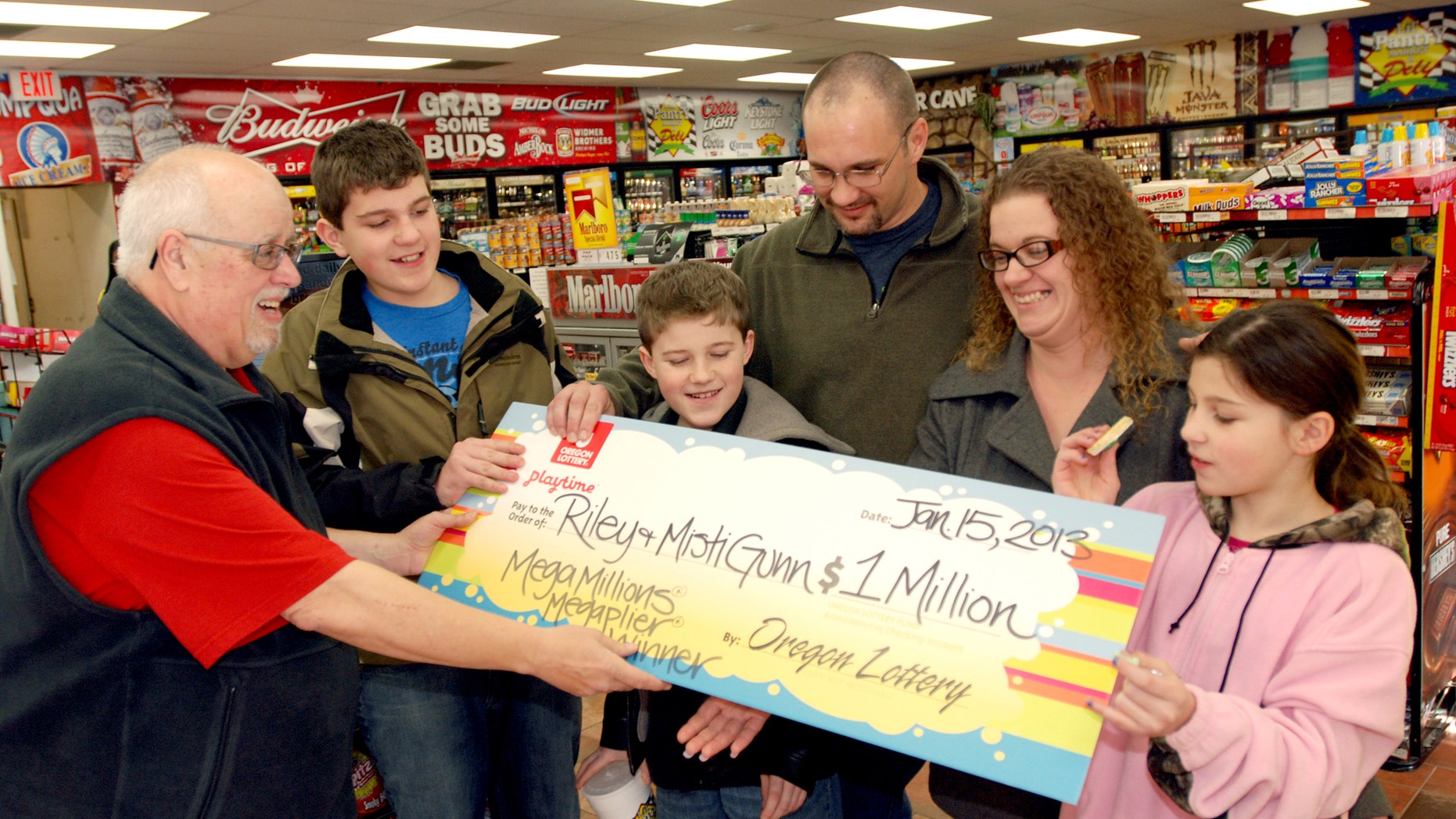 The Gunn family of Wolf Creek, Ore., accepts a symbolic check for $1 million before taxes from Oregon Lottery official Ray Martin on Tuesday, Jan. 15, 2013, at the convenience store where they bought it in Merlin, Ore. Riley Gunn lost his job as a project manager for a telecommunications company in May 2012 and moved his family to a one-room cabin outside Wolf Creek, Ore. While he and his wife were driving home, they pulled off the freeway for corn dogs and pizza pockets and bought an $8 ticket, and won $1 million dollars. Riley and Misti Gunn are at center, with their sons Elijah, 13, left, and Isac, 11, and daughter, Destenie, 9, right. (AP Photo/Jeff Barnard)