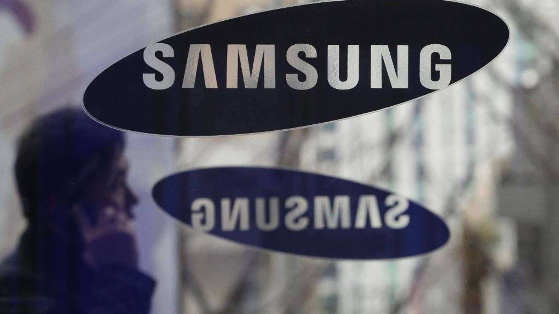 File - In this Dec. 12, 2013 file photo, a man with a mobile phone walks by the Samsung Electronics logos at its headquarters in Seoul, South Korea. Samsung Electronics said Monday, Nov. 14, 2016, it has agreed to acquire auto-systems maker Harman for $8 billion as the South Korean giant eyes the growing market for connected cars. (AP Photo/Ahn Young-joon, File)