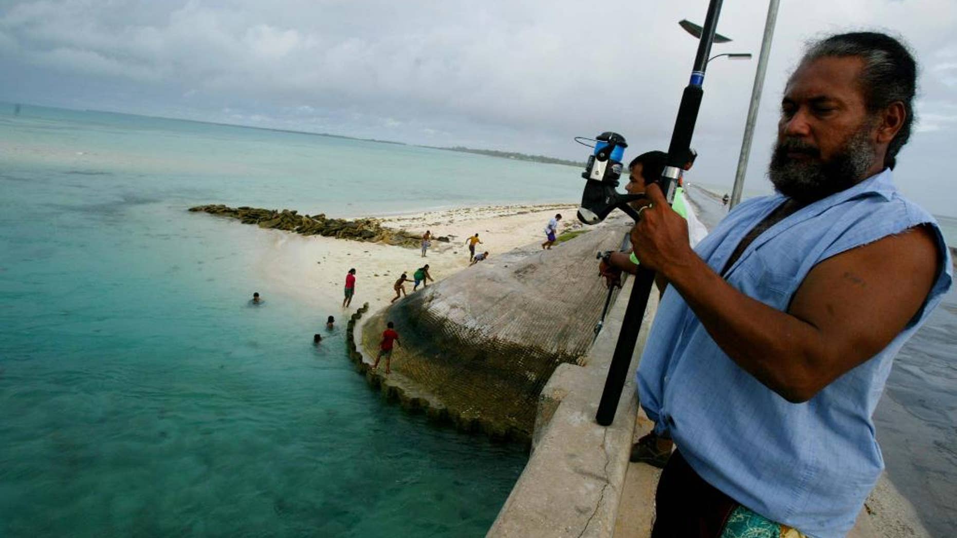 FILE - In this March 30, 2004, file photo, a man fishes on a bridge on Tarawa atoll, Kiribati. The island nation of Kiribati established a large shark sanctuary that will help ensure the creatures are protected across much of the central Pacific. Vice President Kourabi Nenem said at the sanctuary’s launch on Friday, Nov. 18, 2016, that the nation was committed to protecting sharks from exploitation and overfishing. (AP Photo/Richard Voge, File)