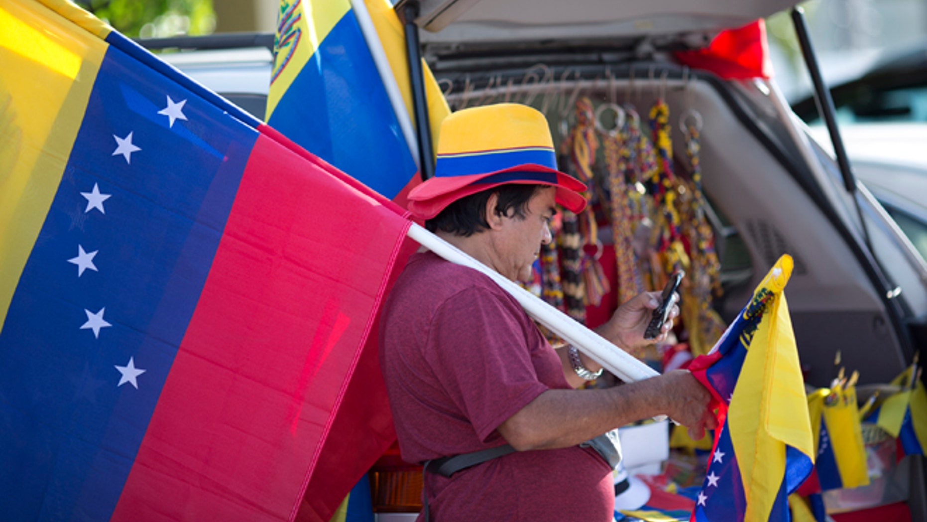 Xidmara Landaeta carries his country's flag, offering them for sale, as Venezuelans from South Florida prepare for their bus trip to Washington, Thursday, May 8, 2014, in Doral, Fla. They are rallying to ask the Congress and President Barack Obama to impose economic sanctions and travel restrictions to the Venezuelan government officials because of presumed human right violations in the South American country. Organizers said they expect Venezuelans from 19 states will meet in Washington on Friday to demonstrate in front of the White House, Congress and the Organization of American States. (AP Photo/J Pat Carter)