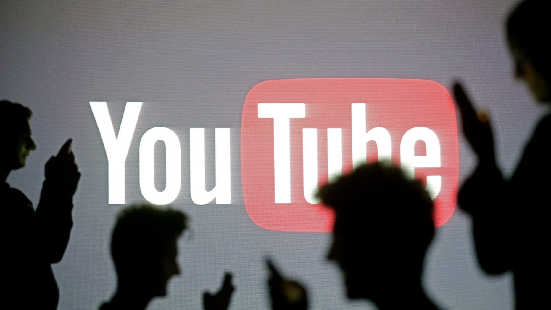 People are silhouetted as they pose with mobile devices in front of a screen projected with a YouTube logo, in this picture illustration taken in Zenica Oct. 29, 2014. (REUTERS/Dado Ruvic)
