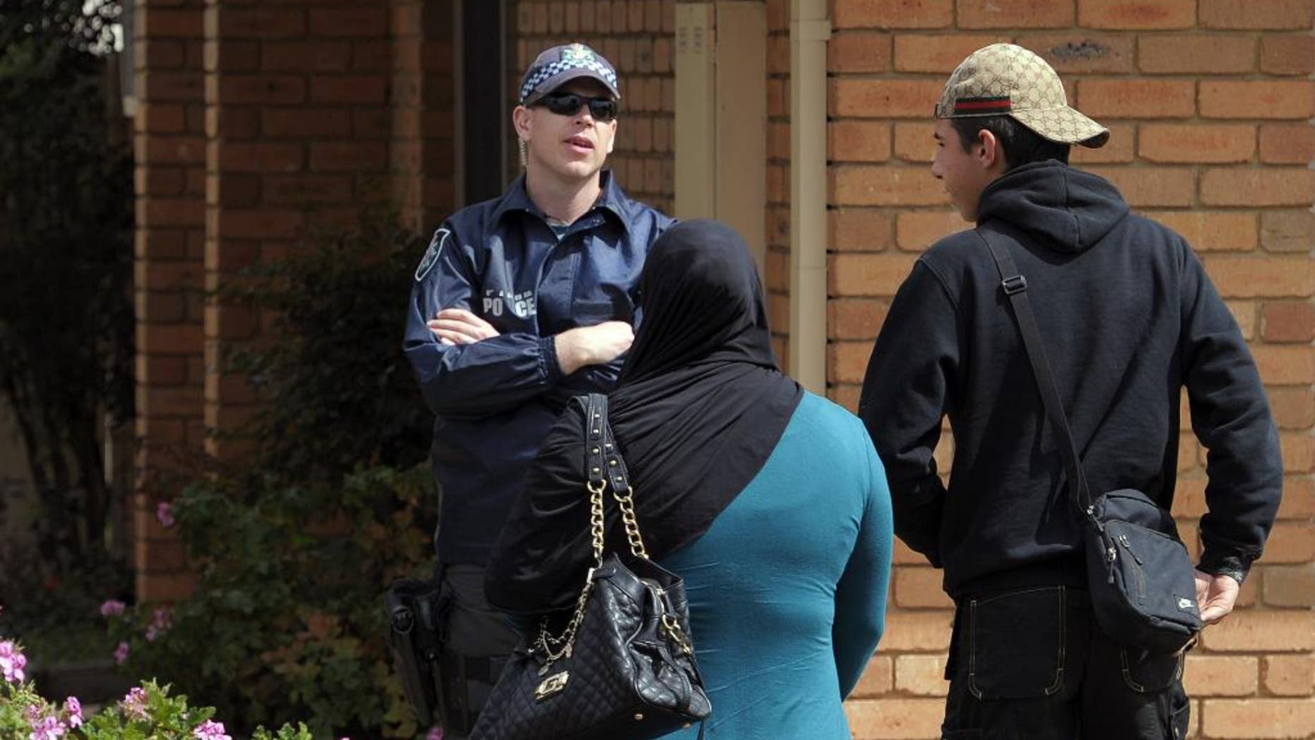 A police officer, left, speaks with two people outside of a house where a man was taken into custody during a counterterrorism raid in Seabrook in suburban Melbourne, Australia, Tuesday, Sept. 30, 2014. The man was arrested after police said he provided money to a U.S. citizen fighting alongside extremists in Syria. (AAP Image/Julian Smith) AUSTRALIA OUT, NEW ZEALAND OUT, PAPUA NEW GUINEA OUT, SOUTH PACIFIC OUT, NO SALES, NO ARCHIVING