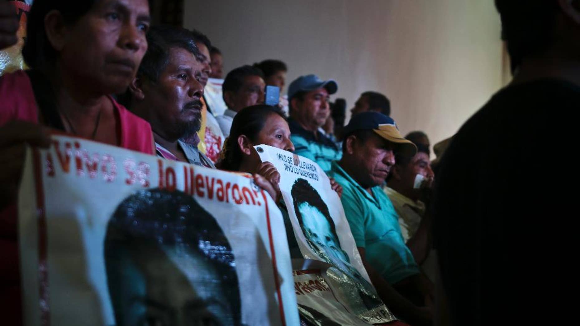 Parents of the 43 teachers' college students hold up images of their missing sons as they listen in to a conference in Mexico City, Sunday, Sept. 5, 2015. An independent report presented Sunday dismantled the Mexican government's investigation into last year's disappearance of the 43 students, saying the prosecutor's contention that they were incinerated in a giant pyre never happened and fueling the anger of parents who still don't know what happened to their sons. (AP Photo/Emilio Espejel)