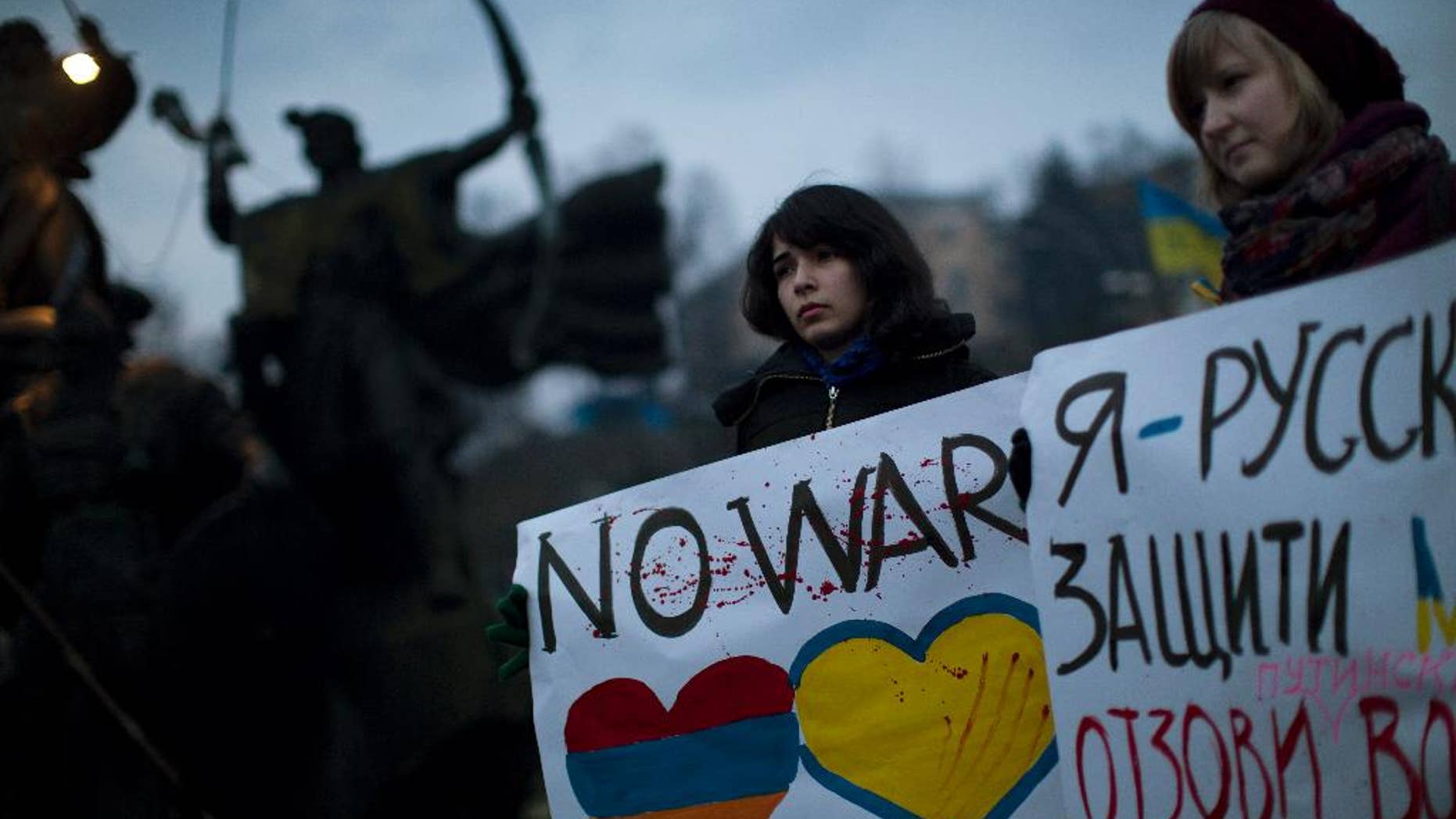 Ukrainian Maria, 23, right, and Vanui, 22, hold posters against Russia's military intervention in Crimea, in Kiev, Ukraine, Sunday, March 2, 2014. Russia's parliament approved a motion to use the country's military in Ukraine after a request from President Vladimir Putin as protests in Russian-speaking cities turned violent Saturday, sparking fears of a wide-scale invasion. The poster in the right side reads in Ukrainian: "I am from Russia, please protect me and remove the weapons and soldiers from Ukraine." (AP Photo/Emilio Morenatti)