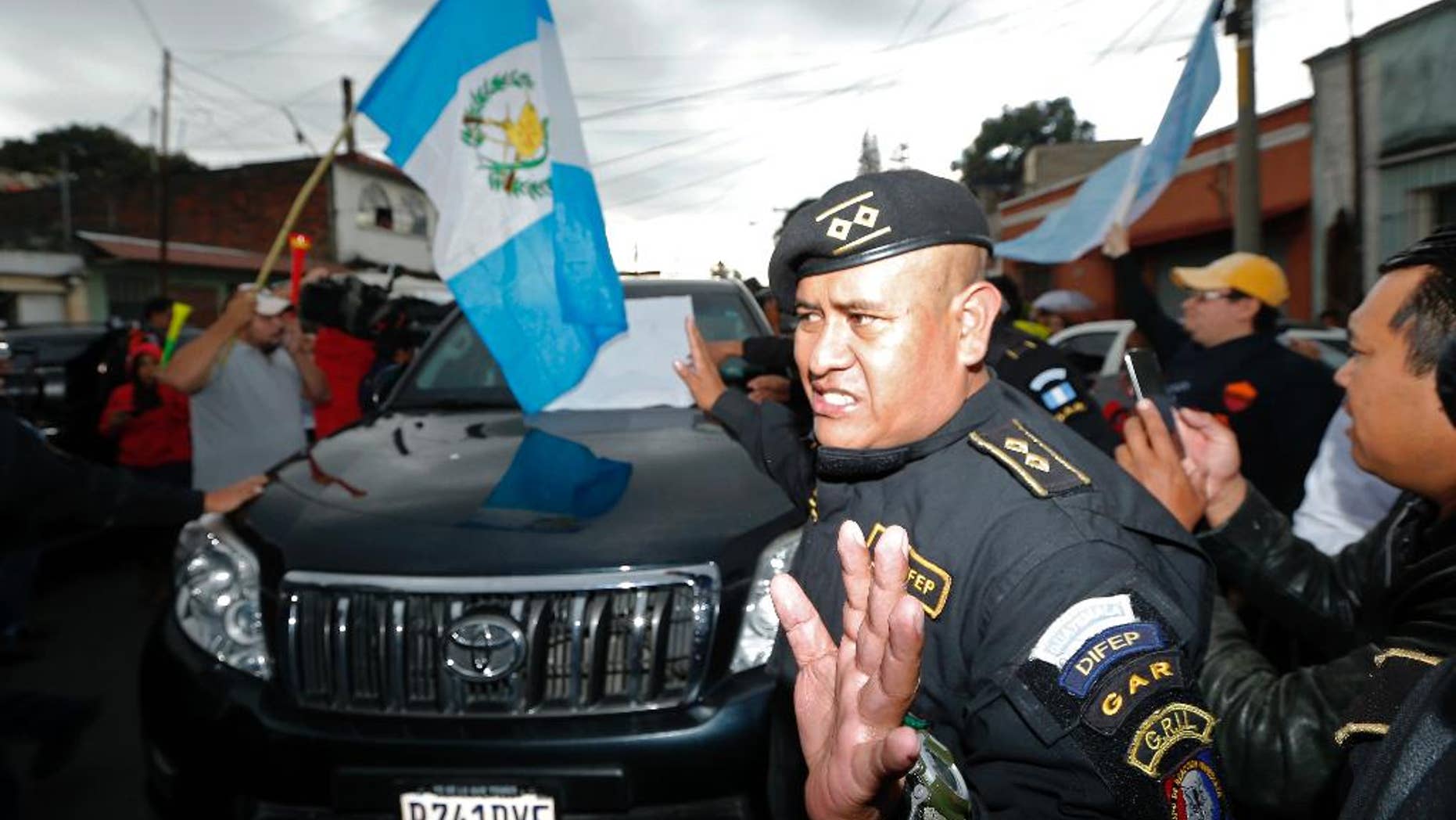 A Guatemalan police officer tries to clear a path for a vehicle carrying former President Otto Perez Molina, as he is transported to the Matamoros military barracks, in Guatemala City, Thursday, Sept 3, 2015. Perez Molina will spend the night in custody before a court hearing into corruption allegations against him reconvenes. He was taken from the court in an SUV and escorted by a dozen police vehicles, initially surrounded by a scrum of media cameras. (AP Photo/Moises Castillo)