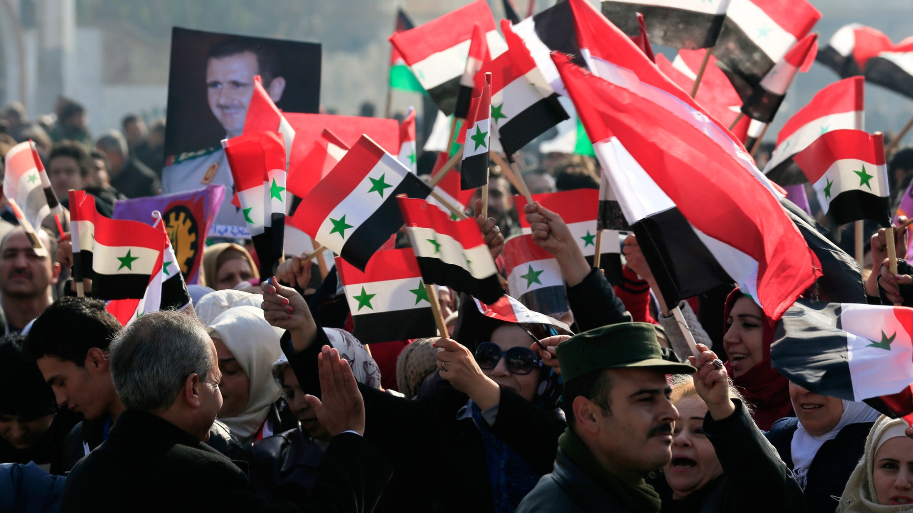 Pro-government supporters hold up the national Syrian flag and pictures of Syrian President Bashar Assad at a gathering at Saadallah al-Jabiri Square in Aleppo, Syria, Thursday, Jan. 19, 2017. Shells slammed into the northern Syrian city of Aleppo Thursday as thousands of government supporters gathered in the main square to celebrate last month's capture of the whole city by the army leading to a disperse by the gathering. (AP Photo/Hassan Ammar)