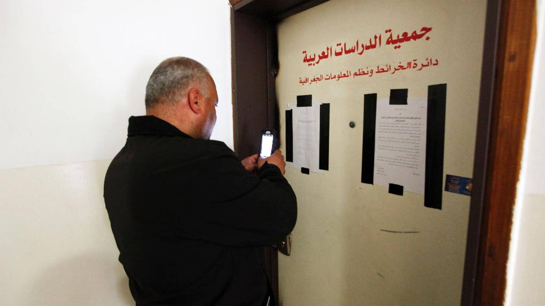 A man takes a photo of the sealed offices of Khalil Tufagji, a prominent Palestinian cartographer, in east Jerusalem, Tuesday, March 14, 2017. Israeli police have raided Tufagji's office accusing him of working illegally on behalf of the Palestinian Authority. In a statement, police accused Tufagji of conducting research for the Palestinian Authority, including gathering information on Israeli development of east Jerusalem. His office is to remain closed for six months. (AP Photo/Mahmoud Illean)