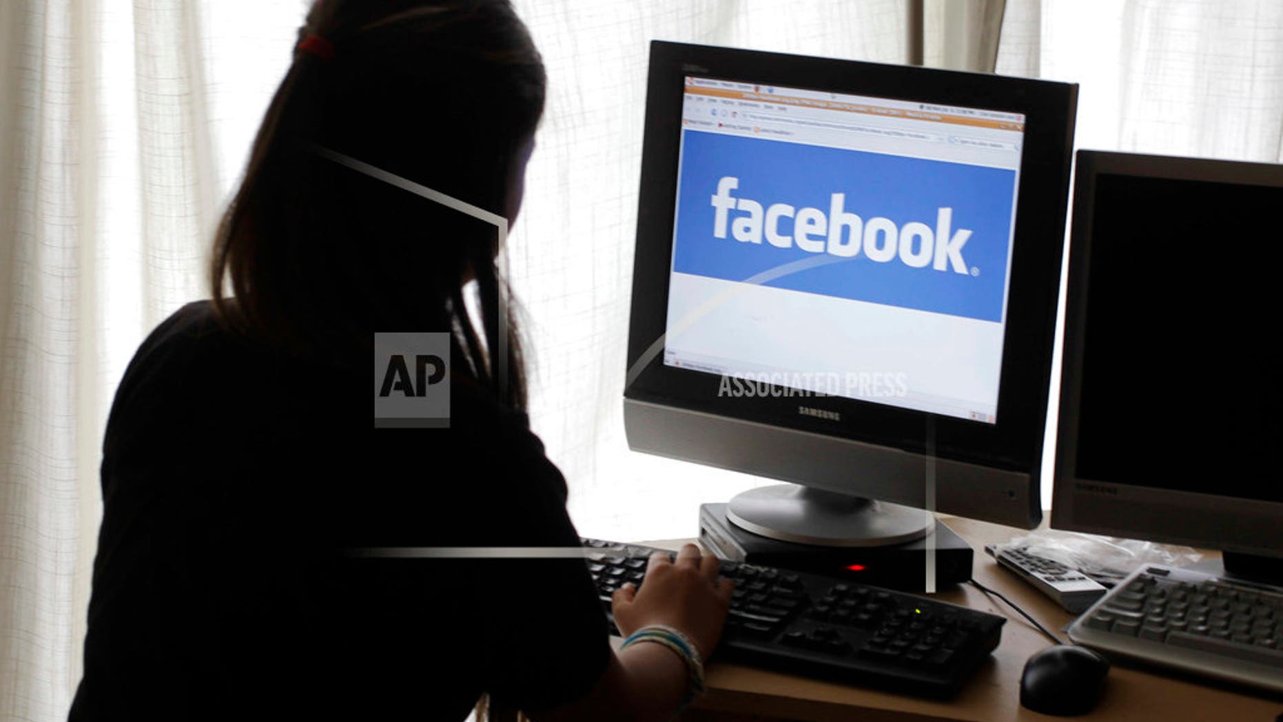 FILE - In this June 4, 2012 file photo, a girl looks at Facebook on her computer in Palo Alto, Calif. Baffled in 2016 by Russian agents who bought ads in an attempt to sway the U.S. presidential campaign, Facebook told the National Association of Secretaries of State on Saturday, Feb. 17, 2018, that the company would send postcards to potential buyers of political ads to confirm they reside in the U.S. The plan was unveiled a day after special counsel Robert Mueller charged 13 Russians with interfering in the presidential election. (AP Photo/Paul Sakuma, File)