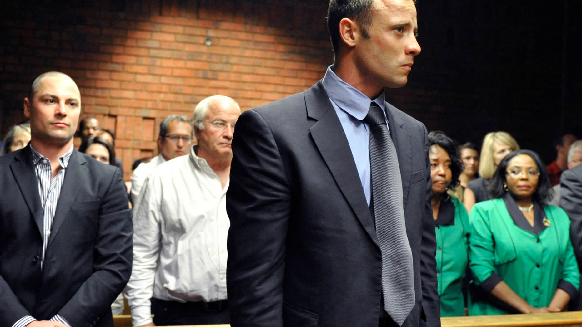 Olympian Oscar Pistorius, foreground, stands following his bail hearing, as his brother Carl, left, and father Henke, second from left, look on in Pretoria, South Africa, Tuesday, Feb. 19, 2013. Pistorius fired into the door of a small bathroom where his girlfriend was cowering after a shouting match on Valentine's Day, hitting her three times, a South African prosecutor said Tuesday as he charged the sports icon with premeditated murder. The magistrate ruled that Pistorius faces the harshest bail requirements available in South African law. He did not elaborate before a break was called in the session. (AP Photo)