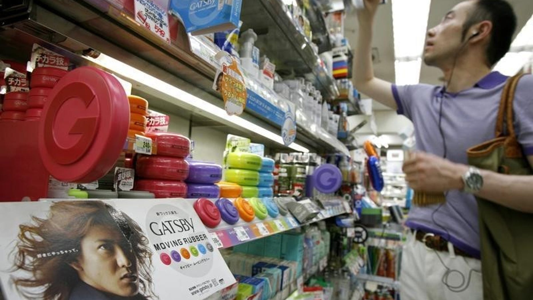 Cosmetics maker Mandom Corp.'s Gatsby "Moving Rubber" hair waxes are seen on a shelf while a man takes a cosmetic product for men at a drug store in Tokyo August 5, 2007. REUTERS/Kiyoshi Ota