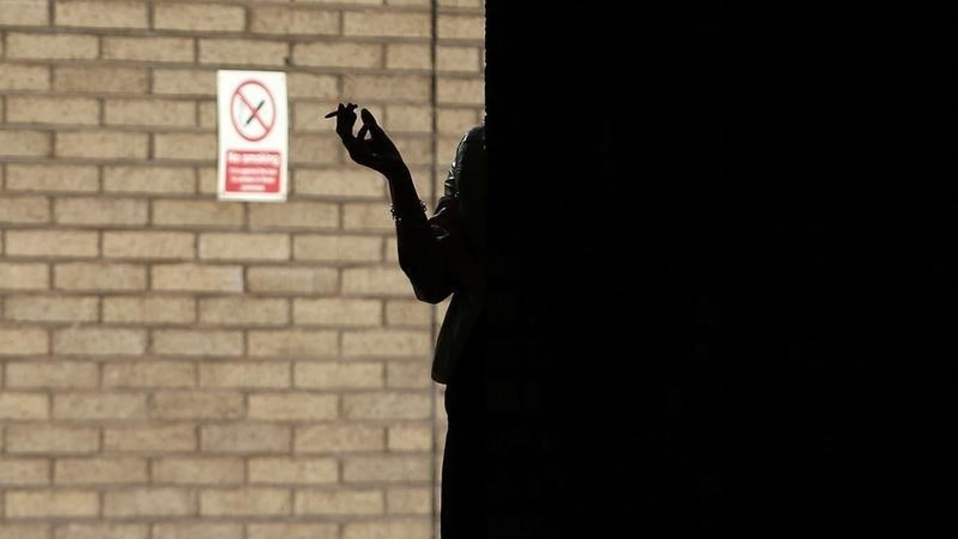 A woman smokes in the shadows outside Southwark Crown Court in central London, March 5, 2014. REUTERS/Andrew Winning
