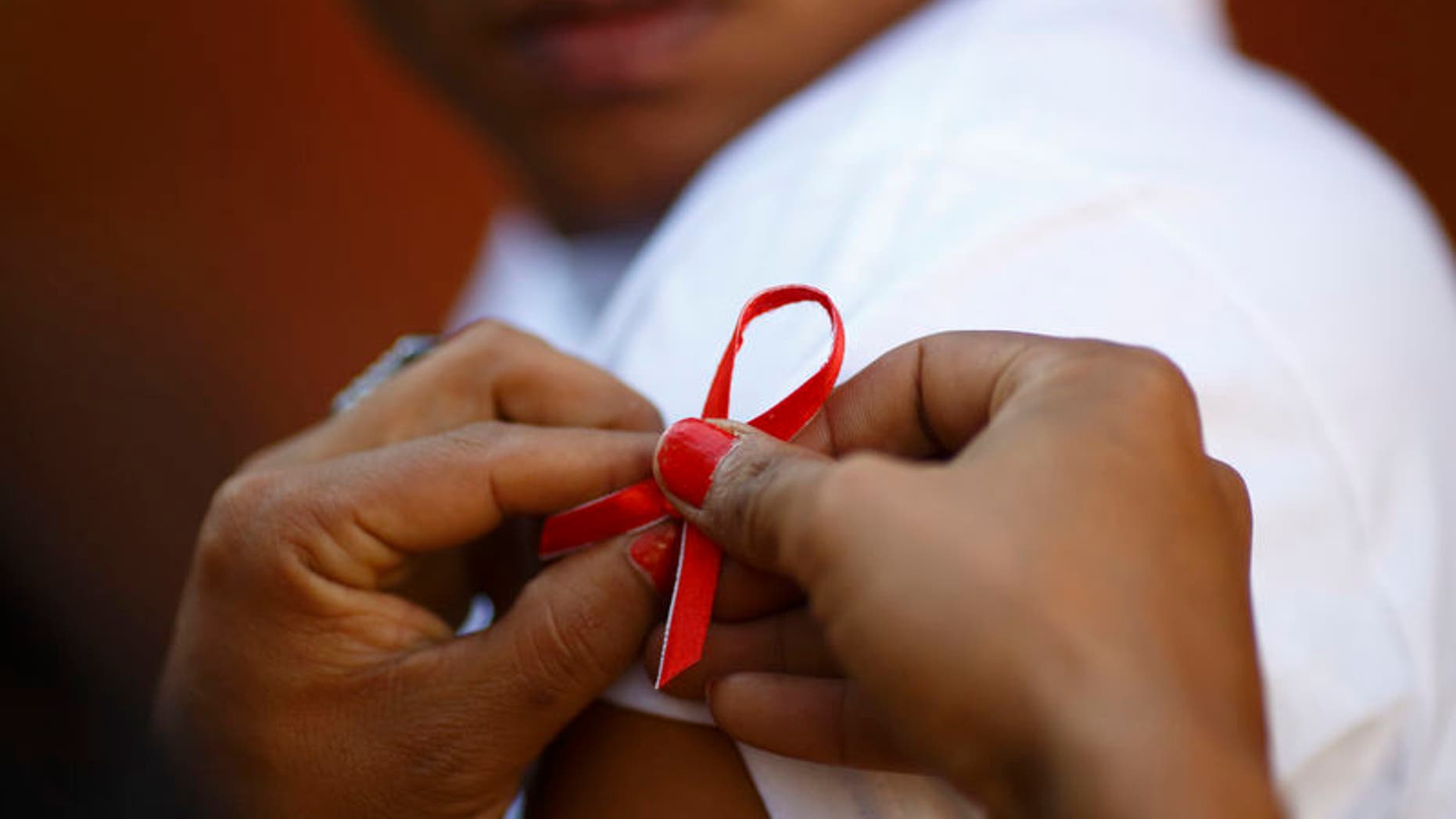 A red ribbon is put on the sleeves of a man by his friend to show support for people living with HIV during a program to raise awareness about AIDS on World AIDS Day in Kathmandu December 1, 2013. REUTERS/Navesh Chitrakar/Files
