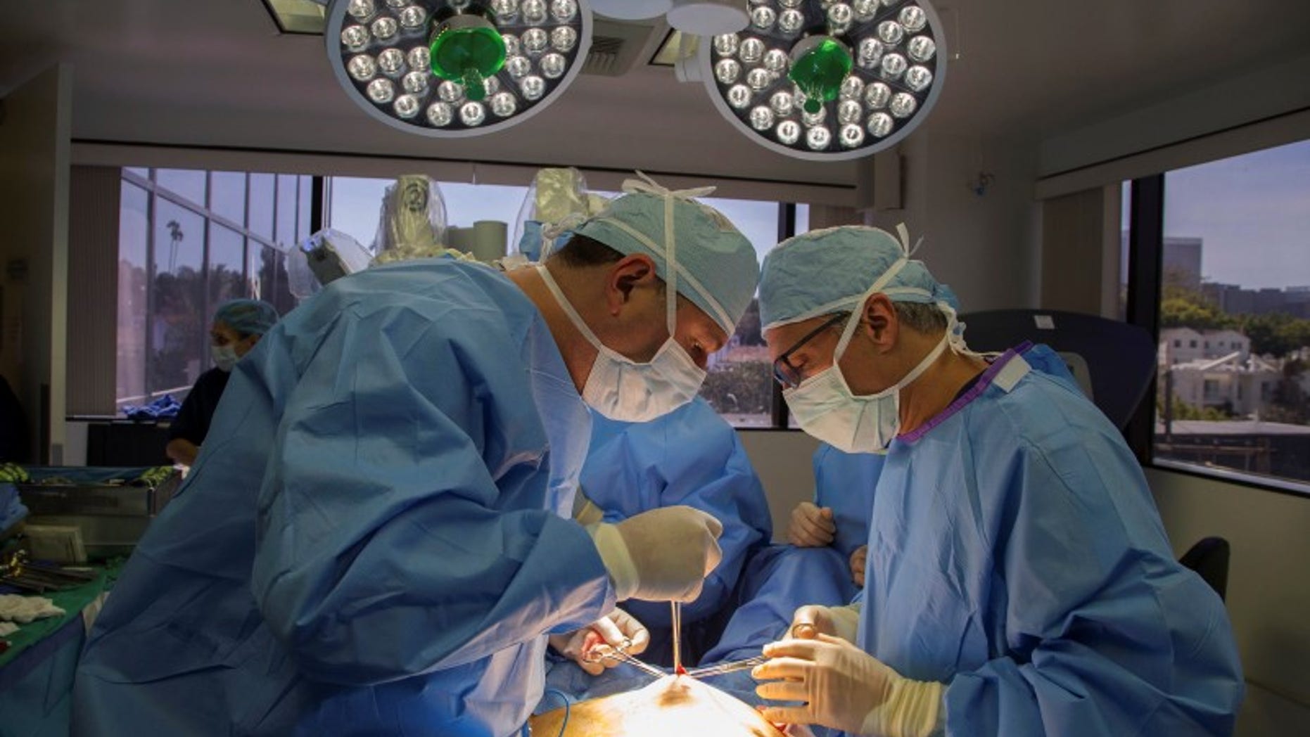 Doctors David Ghozland and Marc Winter make an incision in the belly button of a 49-year-old woman, Sheryl, who had two fibroids, in preparation for a single-site robotic-assisted hysterectomy at miVIP Surgery Center, in Los Angeles, California April 23, 2014. REUTERS/Lucy Nicholson