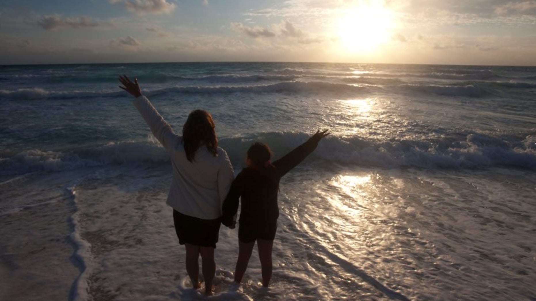 A mother and her daughter raise their hands on a beach at dawn on New Year's Day in Cancun