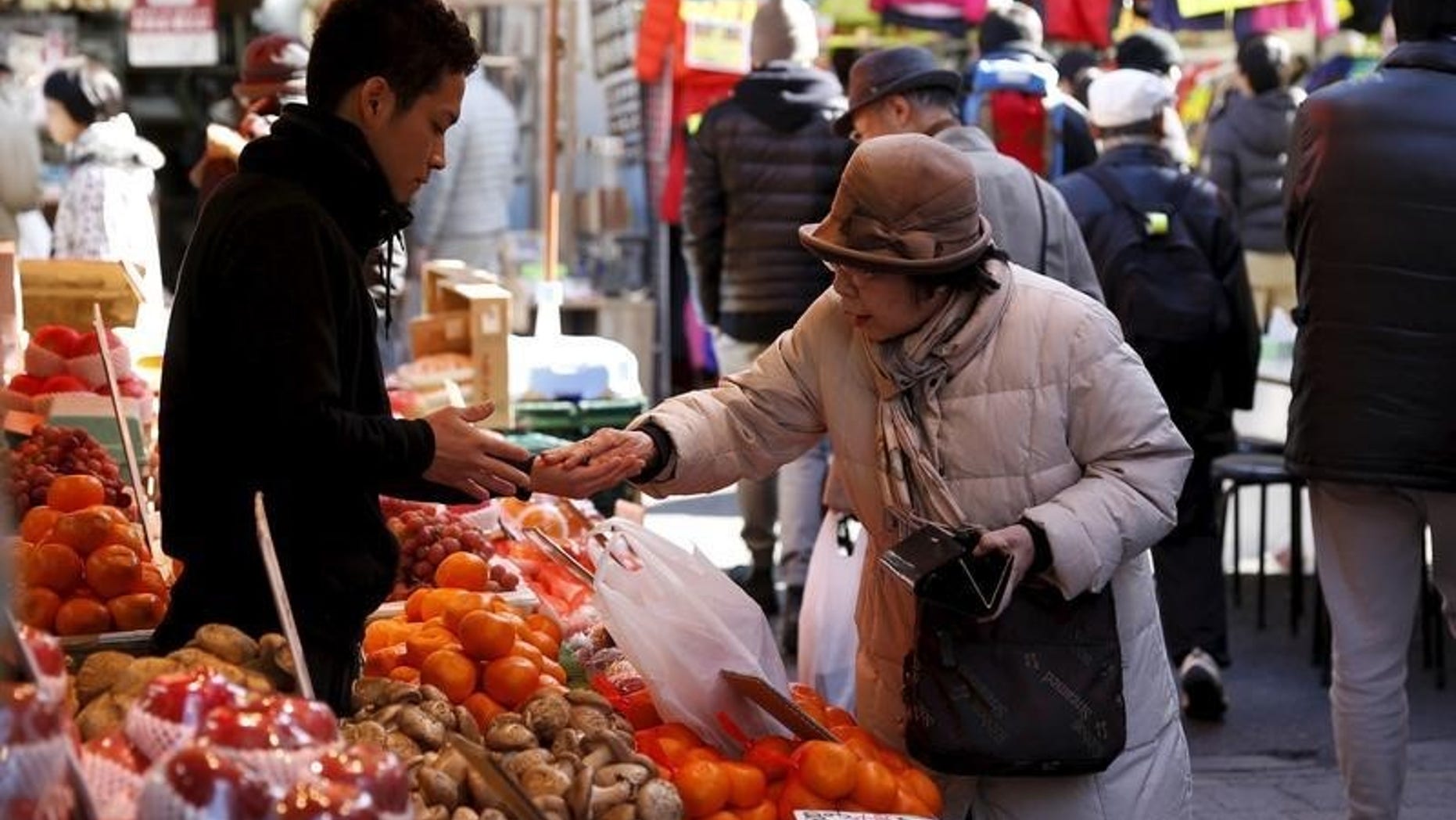 A woman pays money as she buys fruits outside a vegetable store at Ameyoko shopping district in Tokyo
