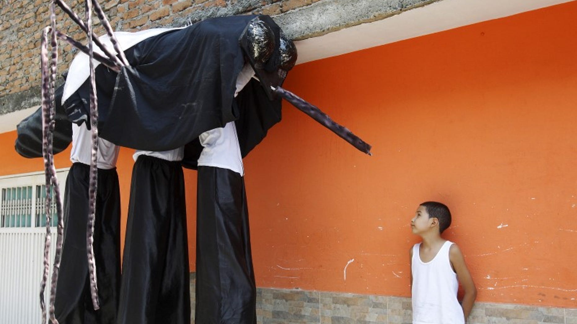 A child looks at men dressed as a mosquito during a health campaign in Cali