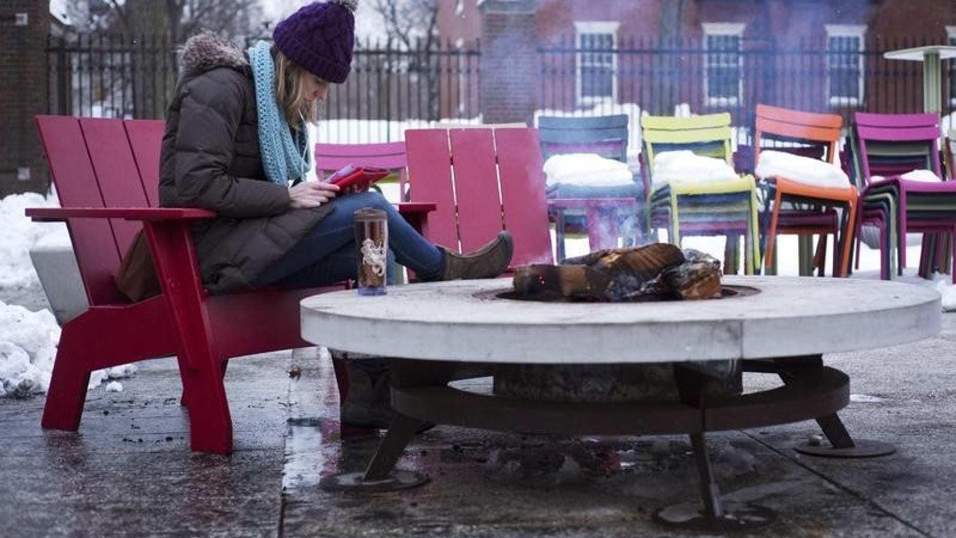 A woman reads a tablet beside a fire pit on cold winter evening outside the Science Center at Harvard University in Cambridge