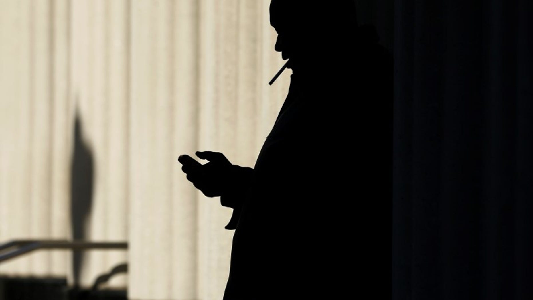 A man sends text messages on his mobile phone as he smokes a cigarette outside the court building in San Diego