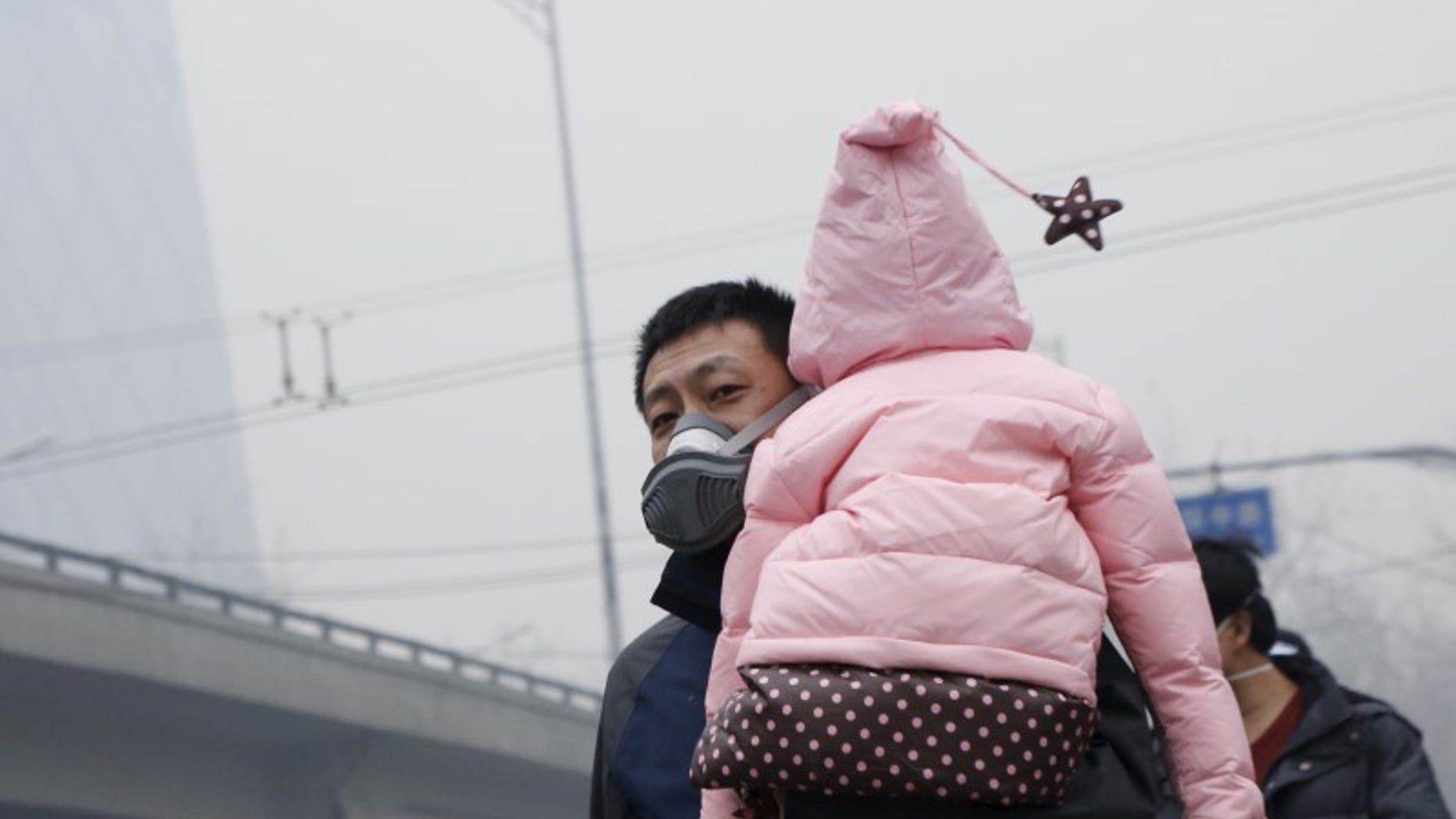 A man wearing a mask carries his baby on his shoulder amid heavy smog after the city issued its first ever "red alert" for air pollution, in Beijing