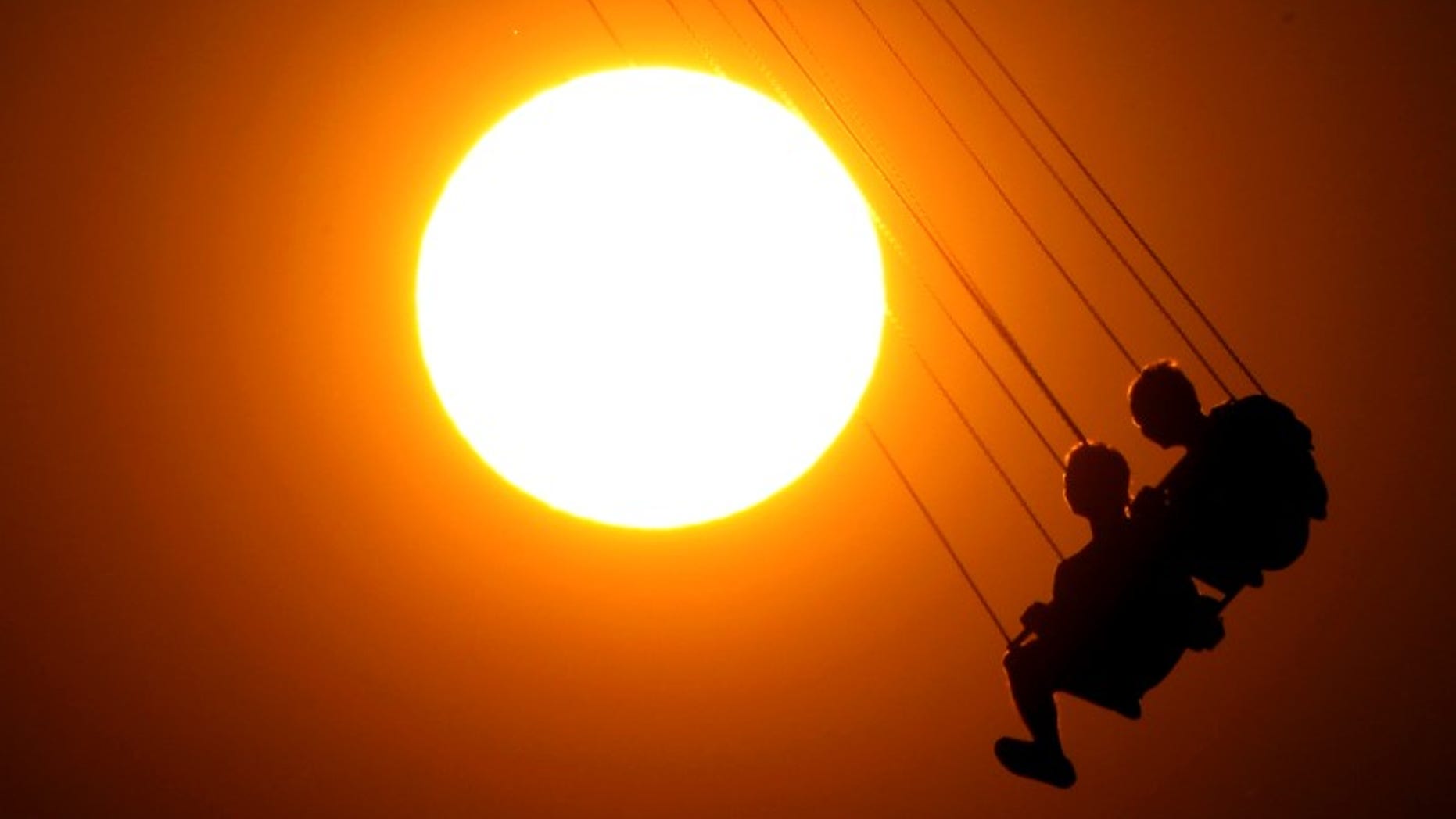 People enjoy a ride on a circular swing at sunset in Athens