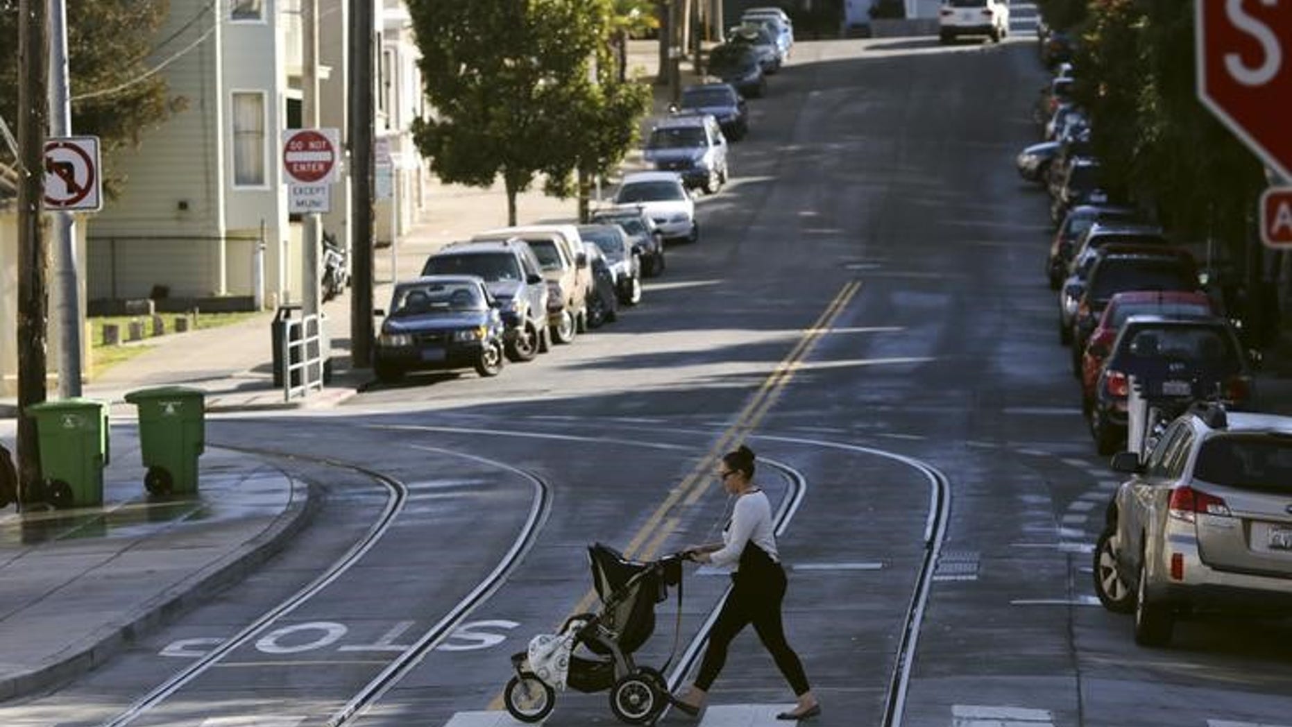 A woman walks with a child stroller across a pedestrian crossing, in San Francisco