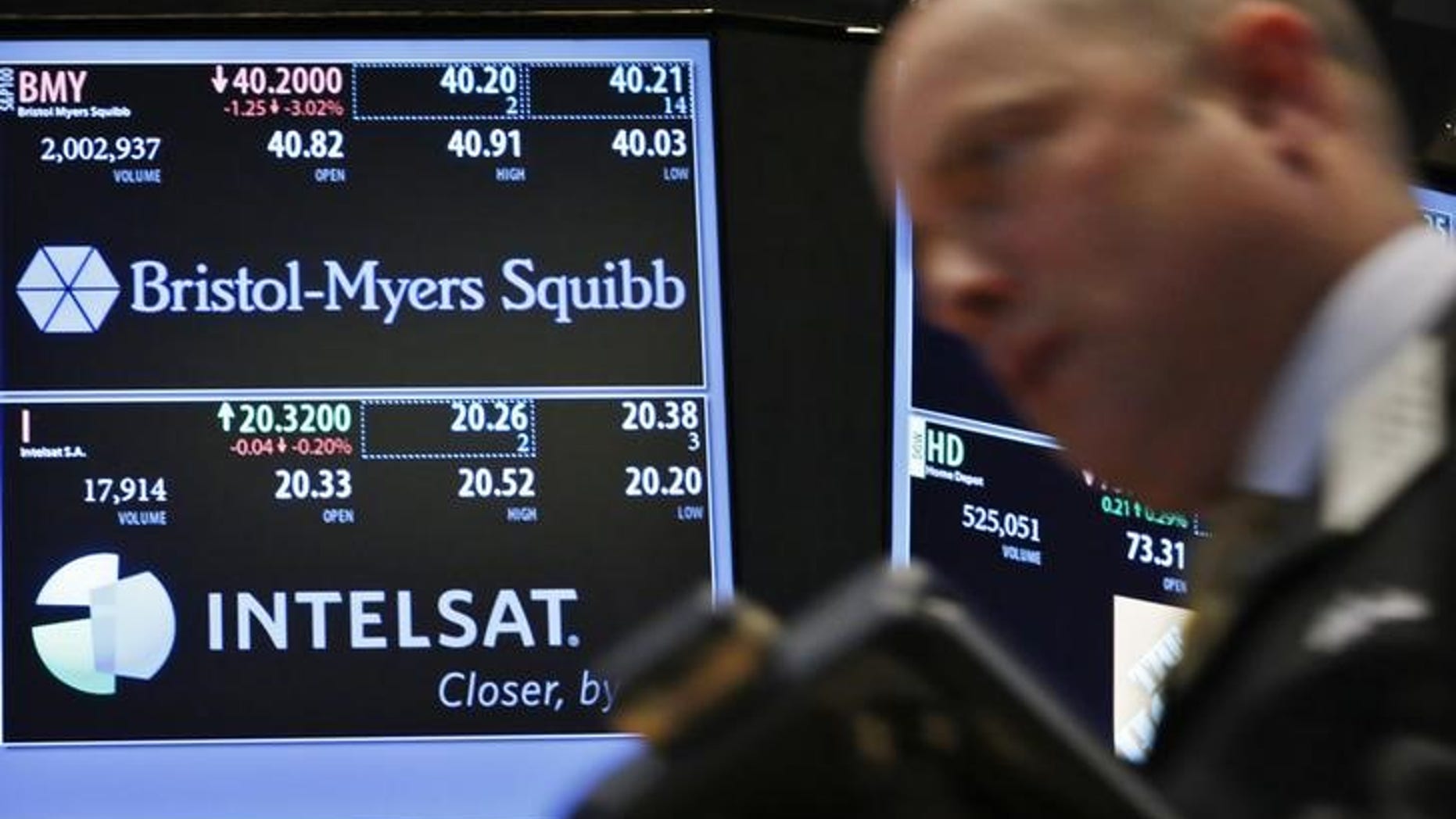A trader passes by a screen displaying the tickers symbols for Bristol-Myers Squibb and Intelsat, Ltd. on the floor at the New York Stock Exchange