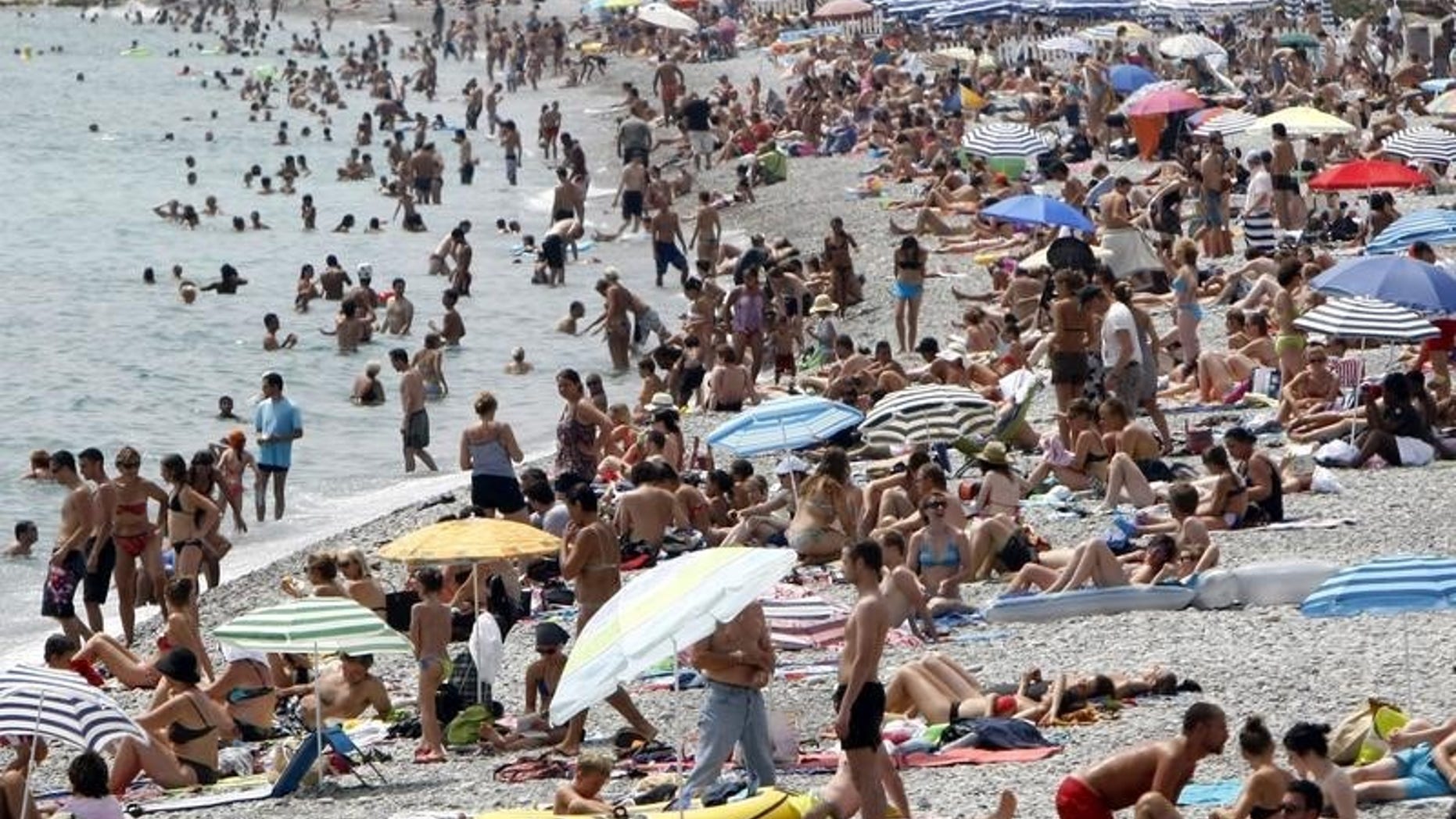 Holidaymakers and tourists sunbathe on the beach on a hot summer day in Nice