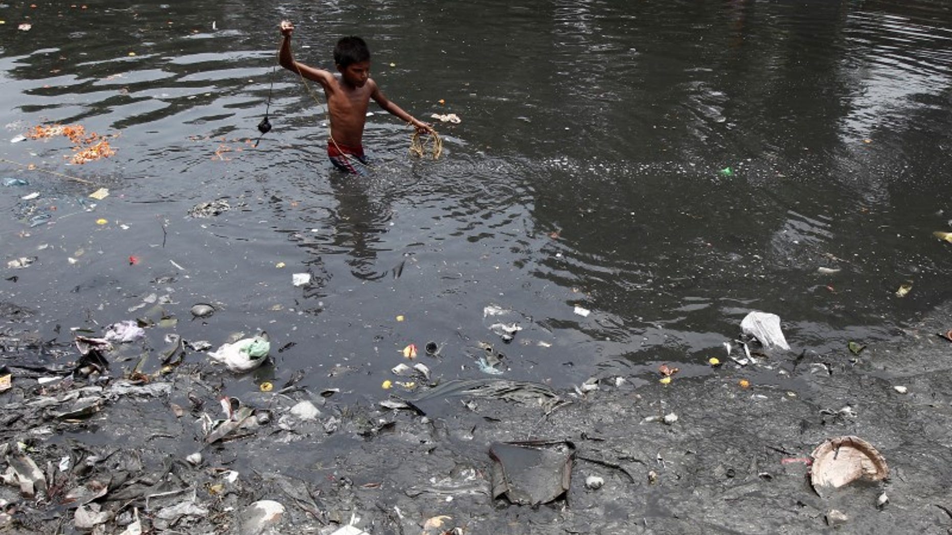 A boy searches for coins thrown by devotees as religious offerings in a polluted water channel near a temple in Kolkata