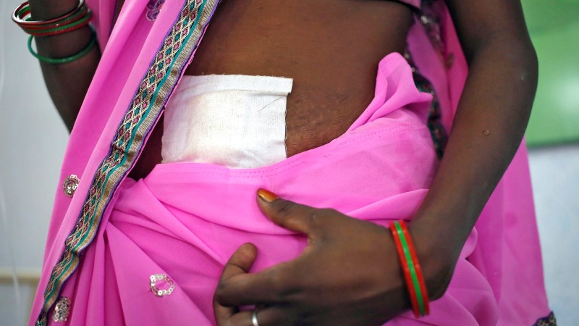 A woman, who underwent sterilization surgery at a government mass sterilisation "camp", walks to sit in a hospital bed at a district hospital in Bilaspur
