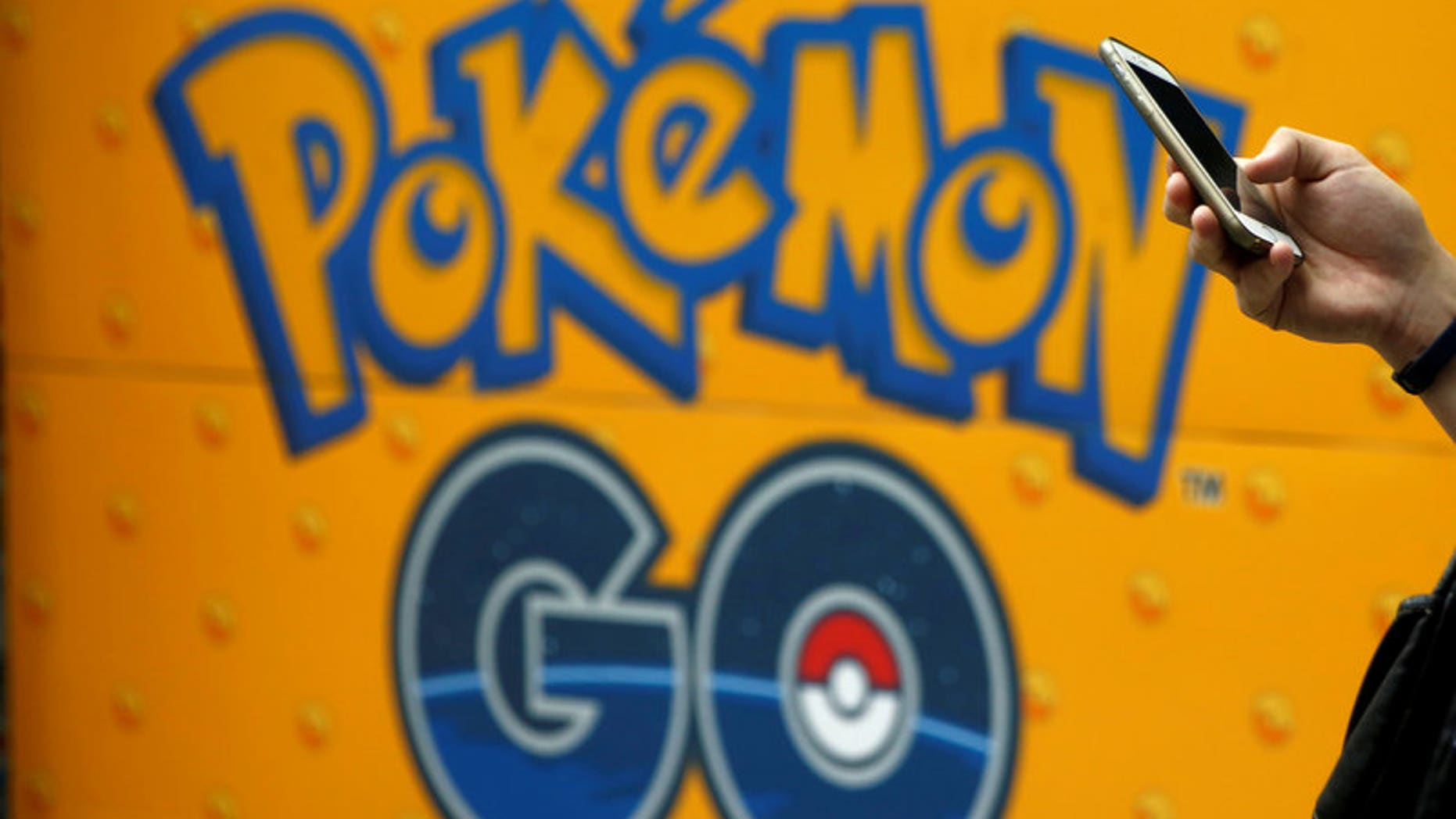 A man uses a mobile phone in front of an advertisement board bearing the image of Pokemon Go at an electronic shop in Tokyo