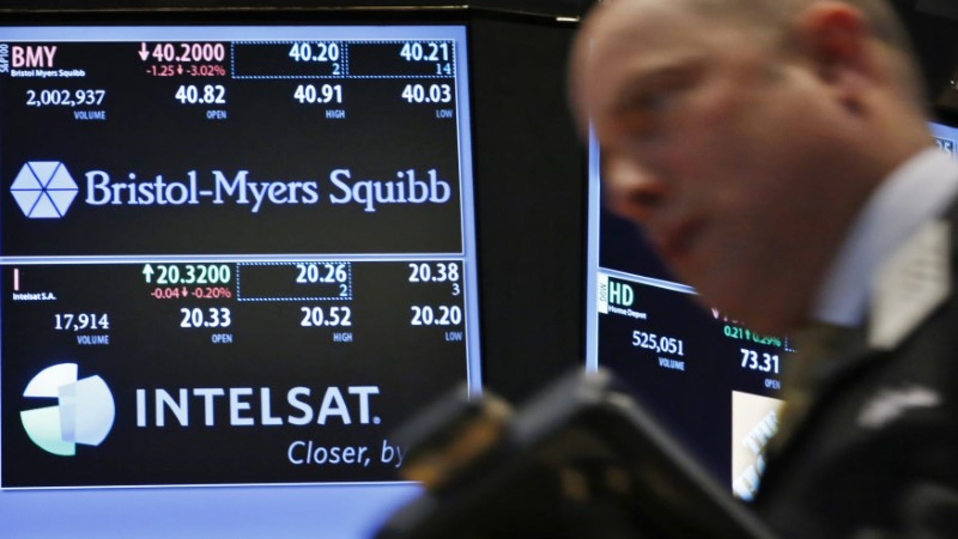 A trader passes by a screen displaying the tickers symbols for Bristol-Myers Squibb and Intelsat, Ltd. on the floor at the New York Stock Exchange