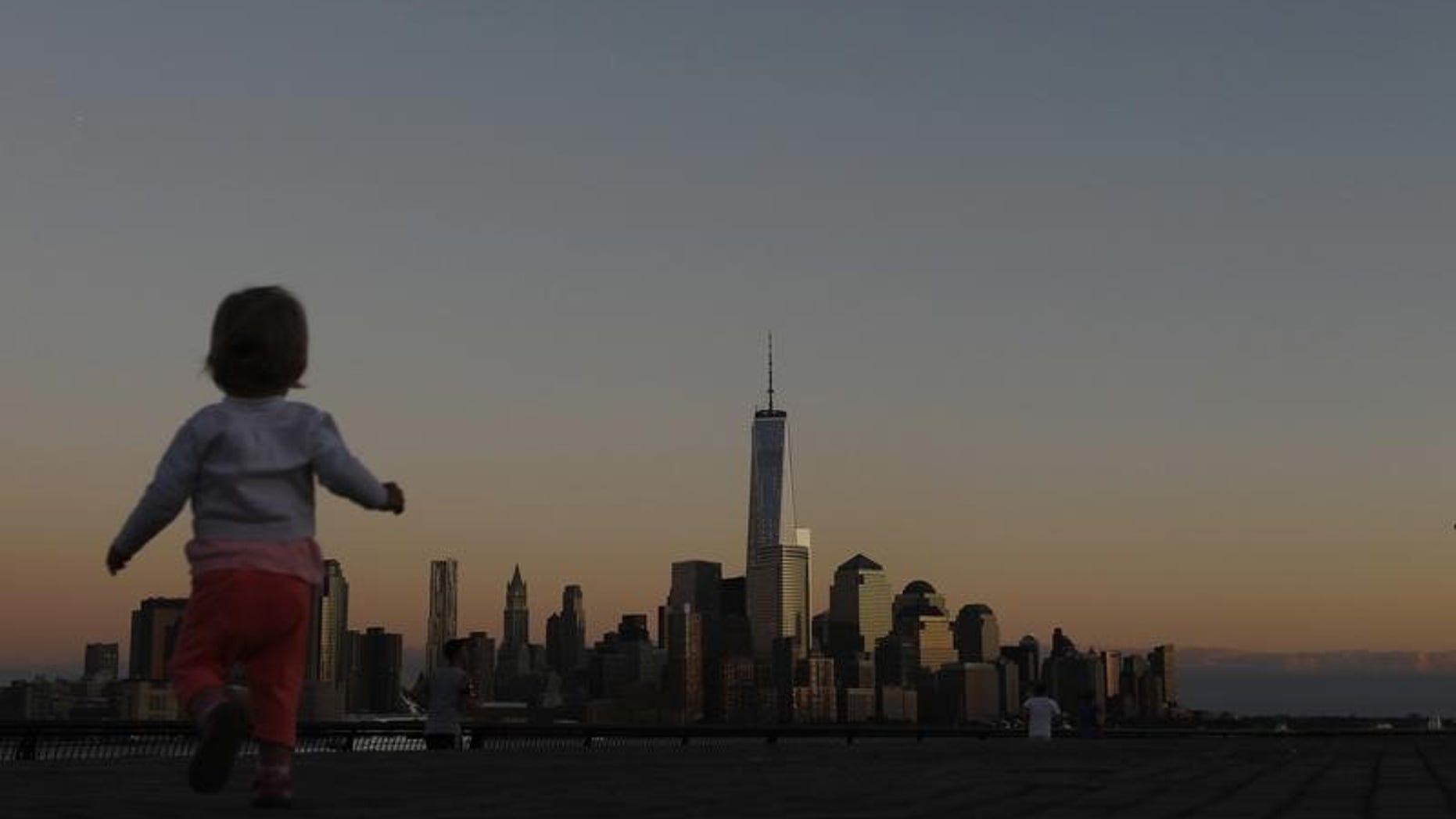 A girl plays in front of the skyline of New York's Lower Manhattan and One World Trade Center in a park along the Hudson River in Hoboken