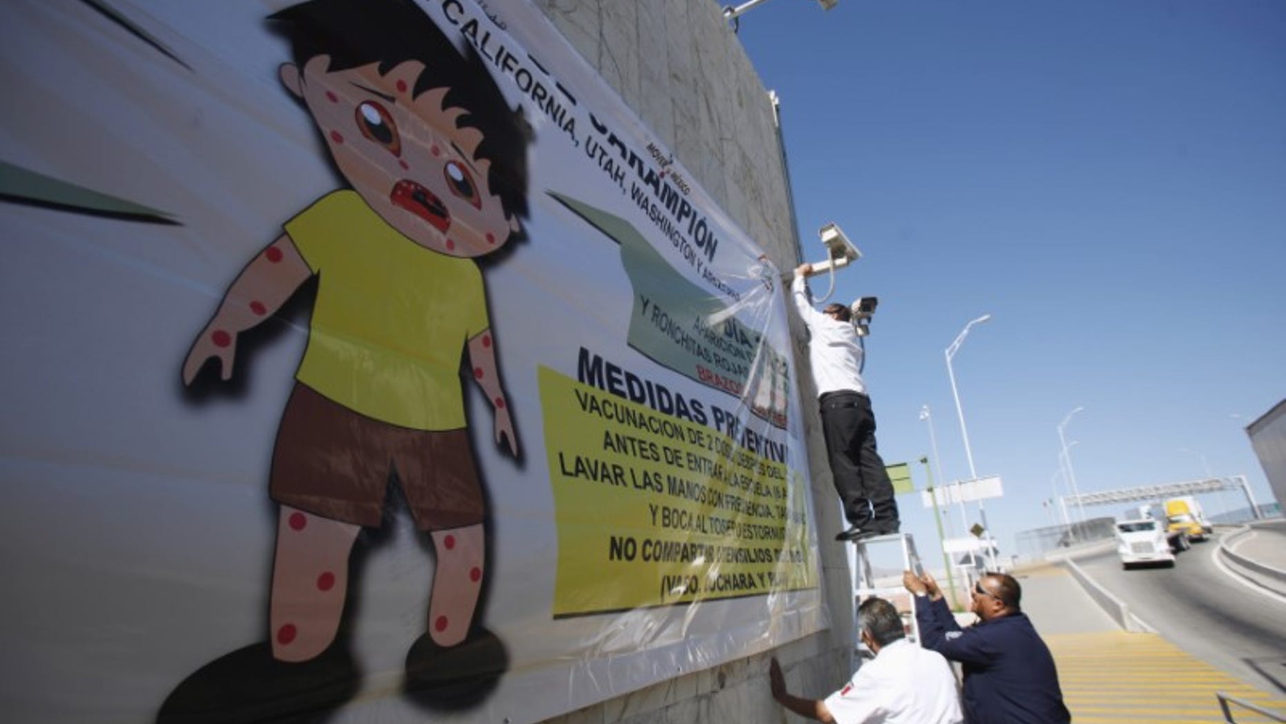 A worker places a banner for a measles prevention programme during an awareness campaign by health workers at the Ciudad Juarez Mexican border crossing with El Paso, Texas