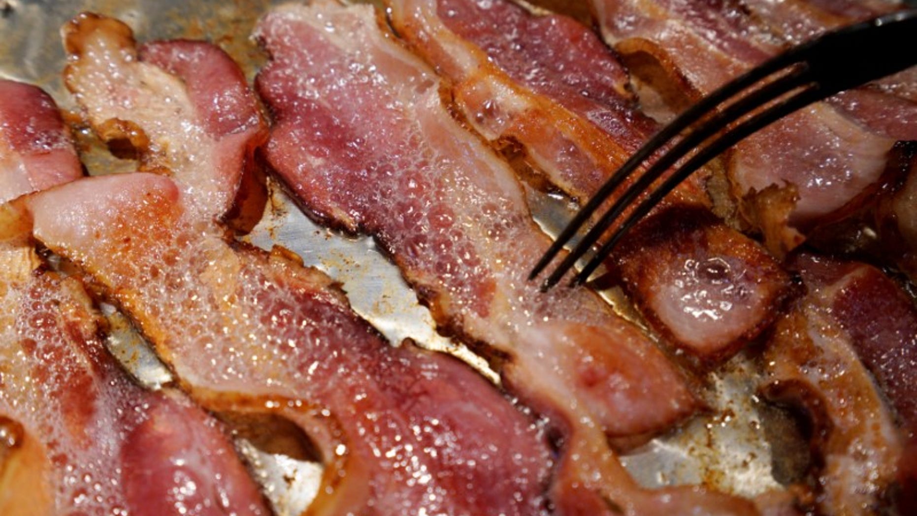 Photo illustration of bacon is fried up in a pan in a kitchen