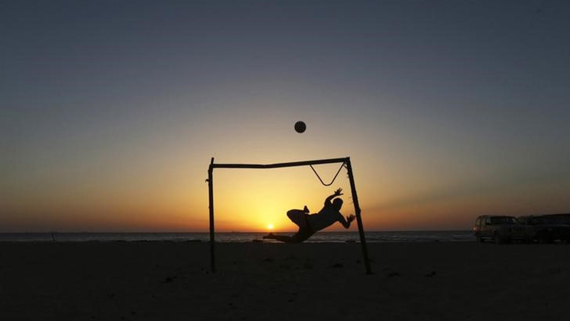 A boy jumps to save a goal while playing soccer on the beach in Benghazi
