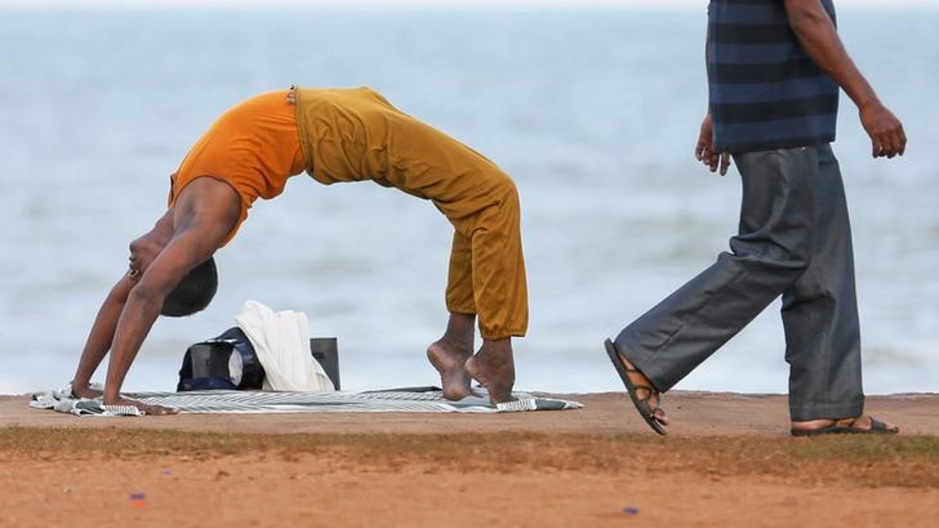 A man performs yoga as another man walks past him at Galle Face Green in Colombo