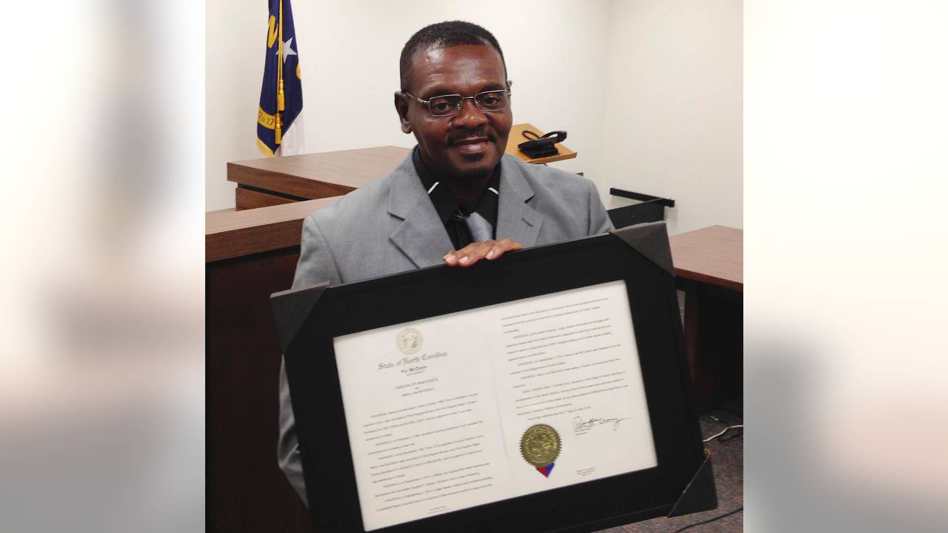 FILE - In this Sept. 2, 2015, file photo, Henry McCollum holds a framed copy of his pardon before a hearing on compensation by the state for his wrongful conviction in Raleigh, N.C. Henry McCollum and Leon Brown wrongfully imprisoned for three decades in the killing of an 11-year-old girl have reached a settlement with investigators who helped put them behind bars. (AP Photo/Jonathan Drew, File)
