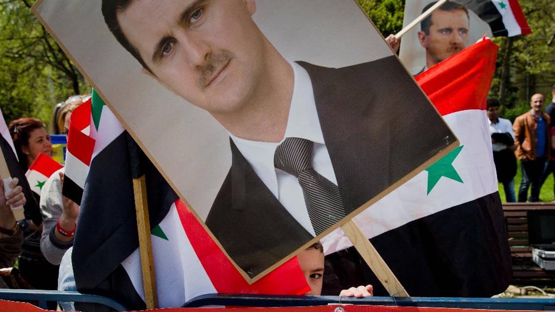 A child of the Syrian community in Romania peers from behind a picture of Syrian President Bashar Assad, during a rally in Bucharest, Romania, Sunday, April 9, 2016. Syrians gathered in a protest against foreign support for the rebel groups in Syria and voiced their support for the country's president Bashar Assad and his regime. (AP Photo/Vadim Ghirda)