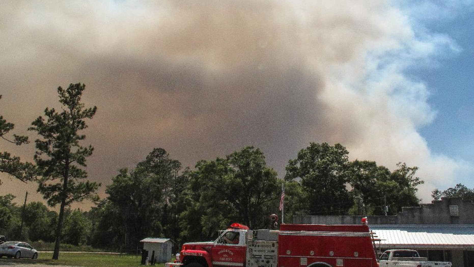 A fire truck passes as a plume of smoke rising from a wildfire burning, Monday, May 8, 2017, just outside the town of St. George, Ga. Officials placed the town under a mandatory evacuation after winds pushed the fire out of the neighboring Okefenokee National Wildlife Refuge, where a lightning strike started the blaze a month earlier. (AP Photo/Russ Bynum)