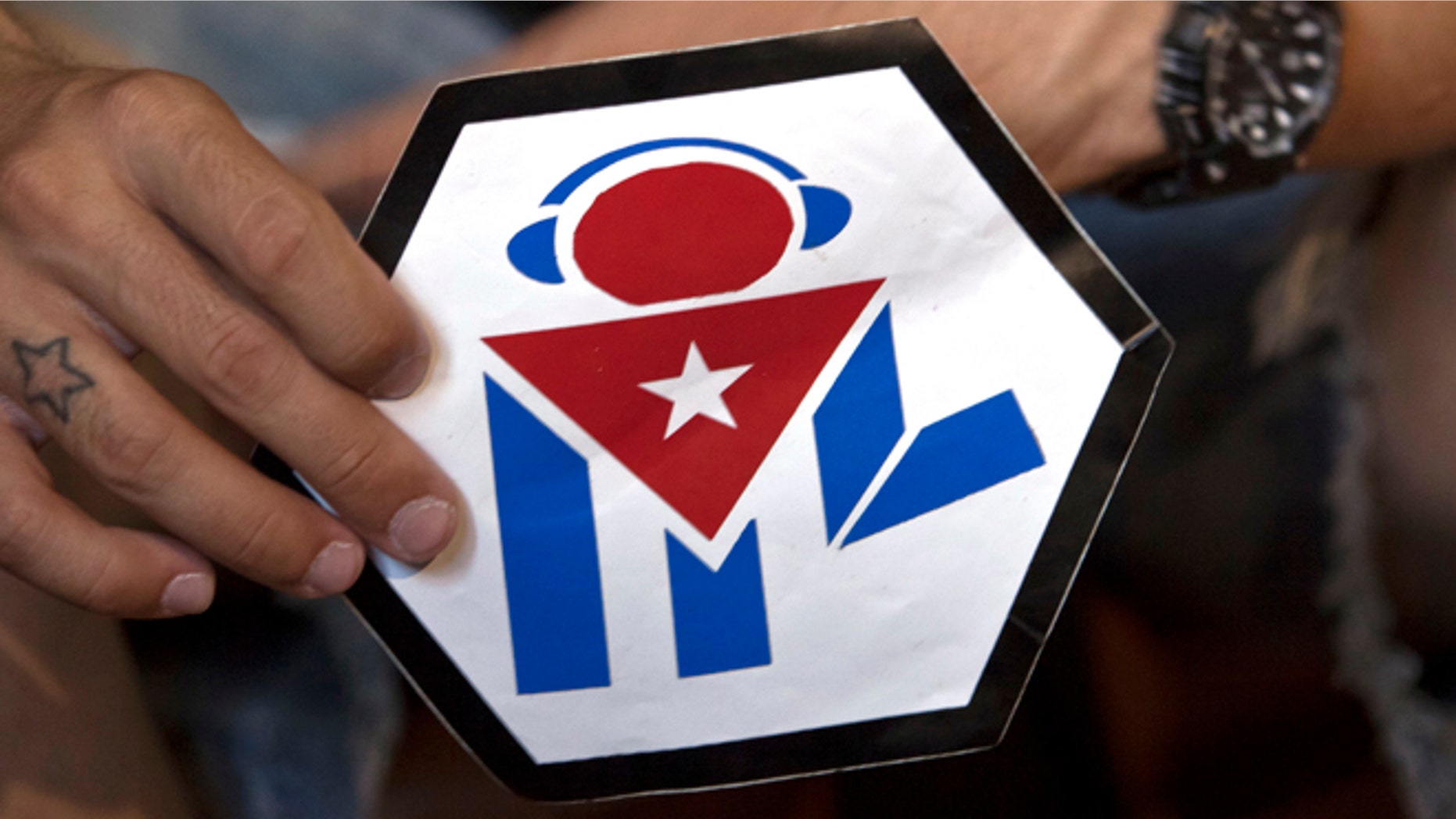 In this July 11, 2014, photo, Manuel Barbosa, 25, shows the logo of his "Revolution" audiovisual project during an interview with The Associated Press in Santa Clara, Cuba. Fernando Murillo contacted Barbosa, a founder of the group, while working on a clandestine operation by the Obama administration that dispatched Latin American youth to Cuba under the cover of health and civic programs to provoke unrest. Barbosa said he was initially open to collaboration with the foreigners but was never told they were working for the U.S. "They presented themselves as a non-governmental organization," Barbosa said. (AP Photo/Franklin Reyes)