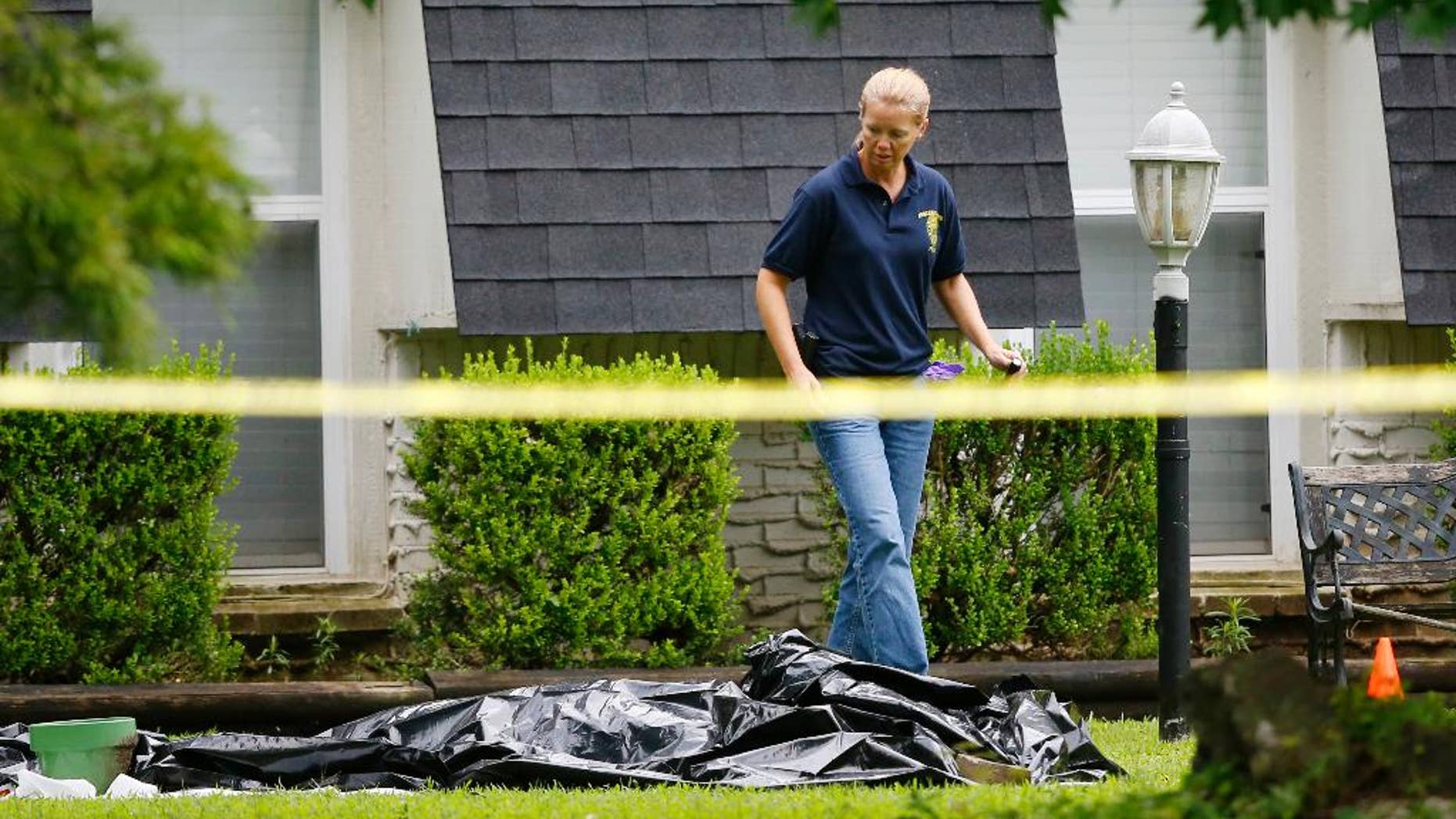 FILE - In this July 23, 2015 file photo, an investigator walks past a tarp covering a body in the front yard of a house in Broken Arrow, Okla. The Oklahoma medical examiner's office says, Monday, July 27, 2015, all five members of a Broken Arrow family killed last week died from multiple sharp-force injuries, and police have said two knives and a small hatchet were found at the scene. (AP Photo/Sue Ogrocki, File)
