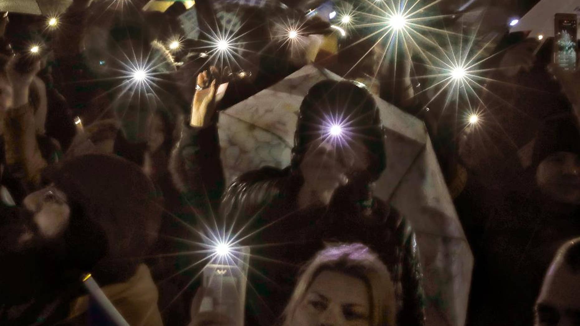 Protesters shine lights of their mobile phones while singing the national anthem outside the government headquarters in the rain in Bucharest, Romania, Sunday, Feb. 19, 2017. Braving the bad weather thousands gathered for the twentieth consecutive day to demand the government's resignation after it passed a decree, since withdrawn, that would have softened the corruption fight that has targeted top officials. (AP Photo/Vadim Ghirda)