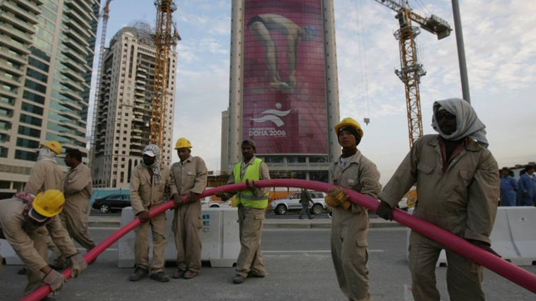 An advertisement for the 15th Asian Games towers over workers in Doha on November 28, 2006