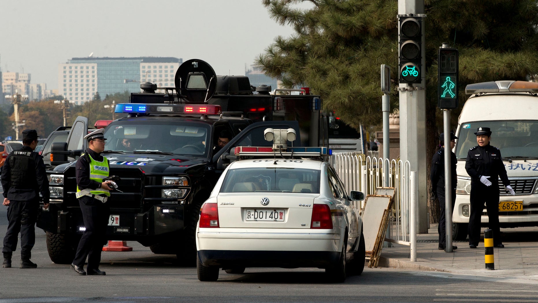 Oct. 30, 2013: Two policewomen, right, a traffic police, in yellow vest, and members of a SWAT team guard a street corner, where, on Monday, a sport utility vehicle veered into a crowd near Tiananmen Gate, where the car crashed and caught fire, in Beijing, China. Chinese police are circulating a list of eight suspects wanted in connection with the apparent suicide car crash near Tiananmen Square in Beijing that killed five people and injured dozens, a hotel manager said Wednesday.