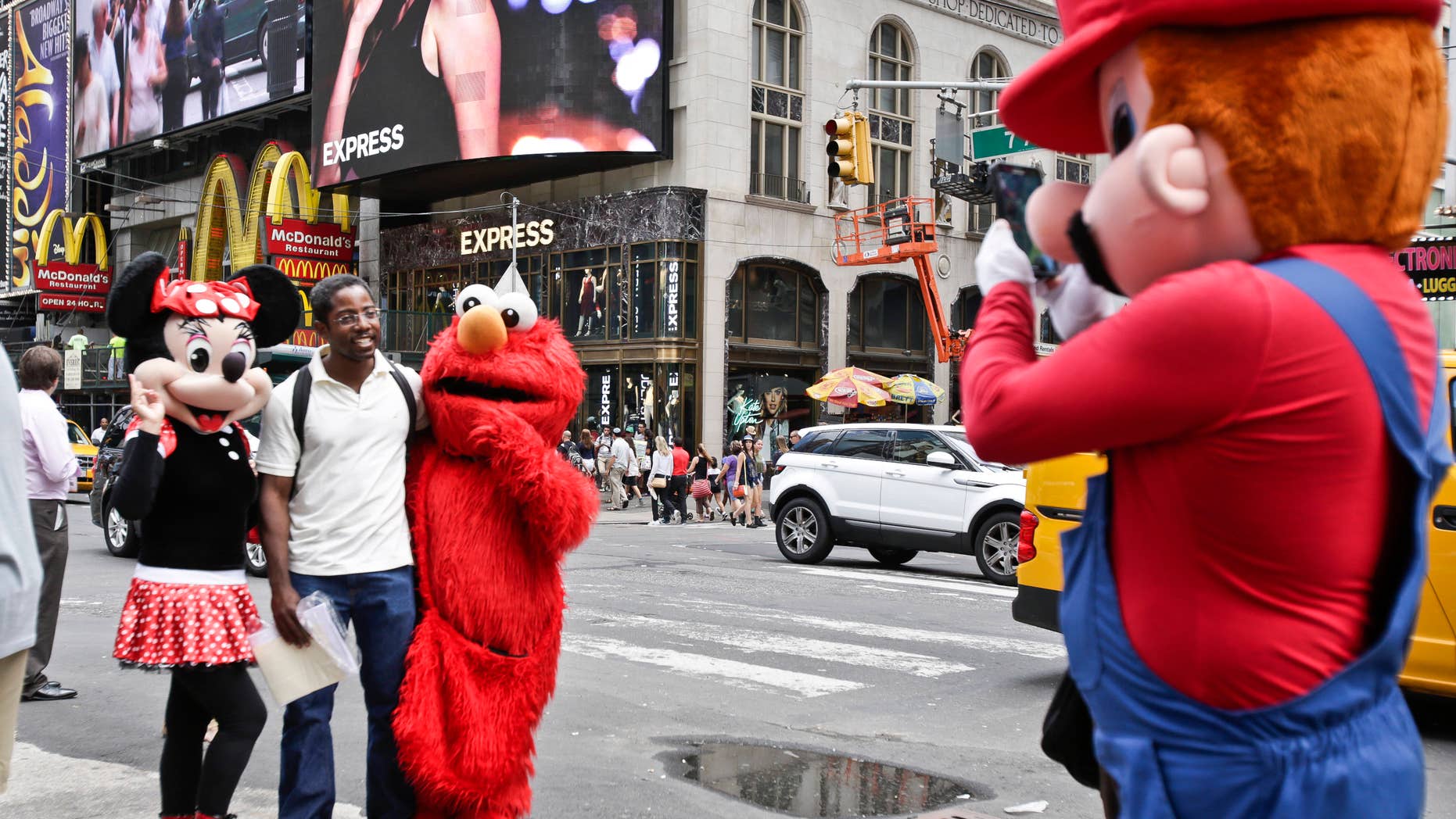 A visitor to Times Square poses for photos with iconic costumed characters, Monday, July 28, 2014, in New York. New York Mayor Bill de Blasio said Monday that he believes the people wearing character costumes in Times Square should be licensed and regulated. (AP Photo/Rachelle Blidner)
