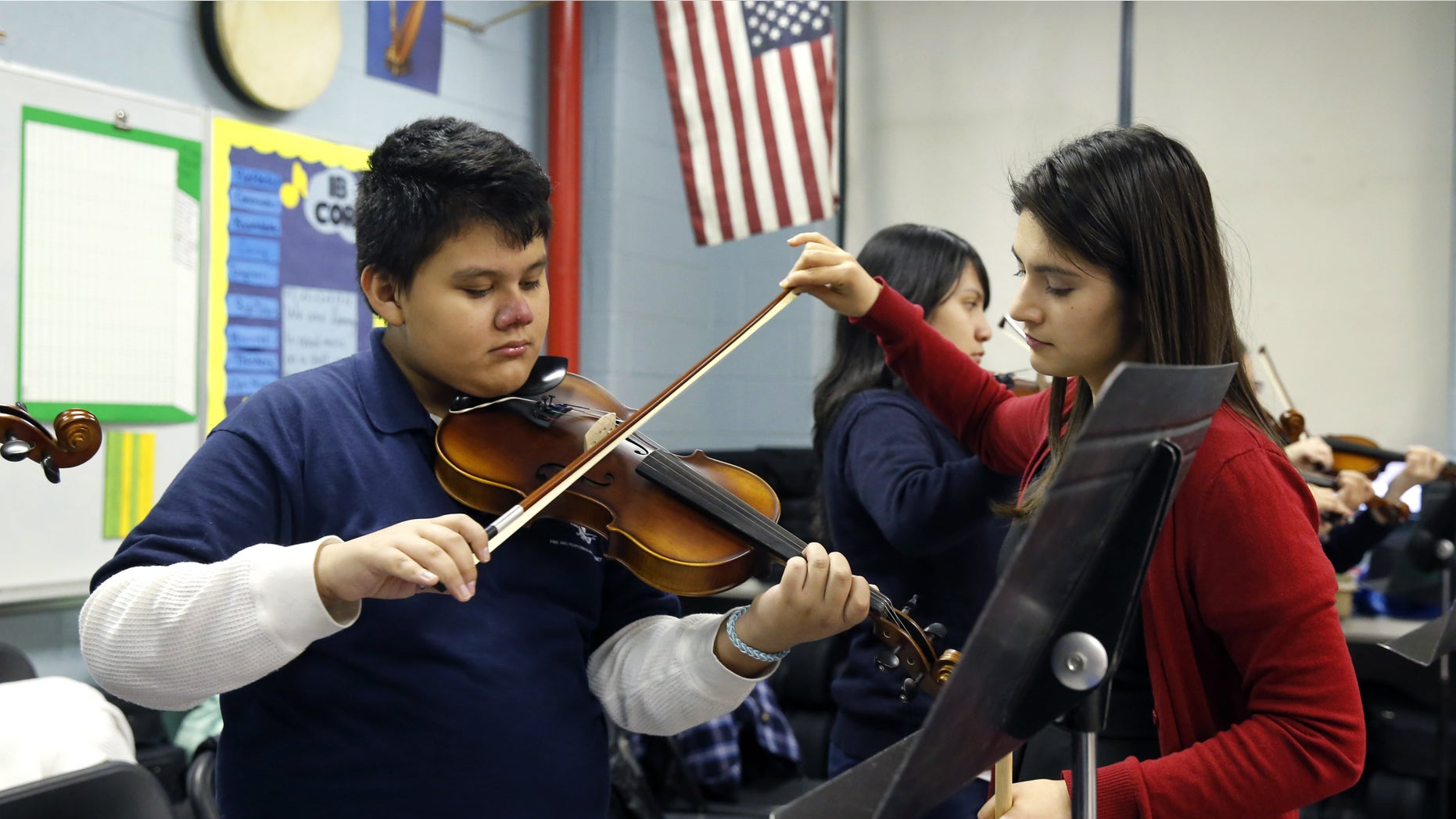 FILE - In this Dec. 12, 2014 file photo, music teacher Maria Pulido, right, works with Brian Gonzalez on his violin at the Richard Edwards Elementary School in Chicago, Illinois. Chicago now joins dozens of school districts across the country that teach mariachi music in schools. It's a way to connect schools and parents, many who speak Spanish, from Hispanic communities, say organizers. (AP Photo/Charles Rex Arbogast, File)