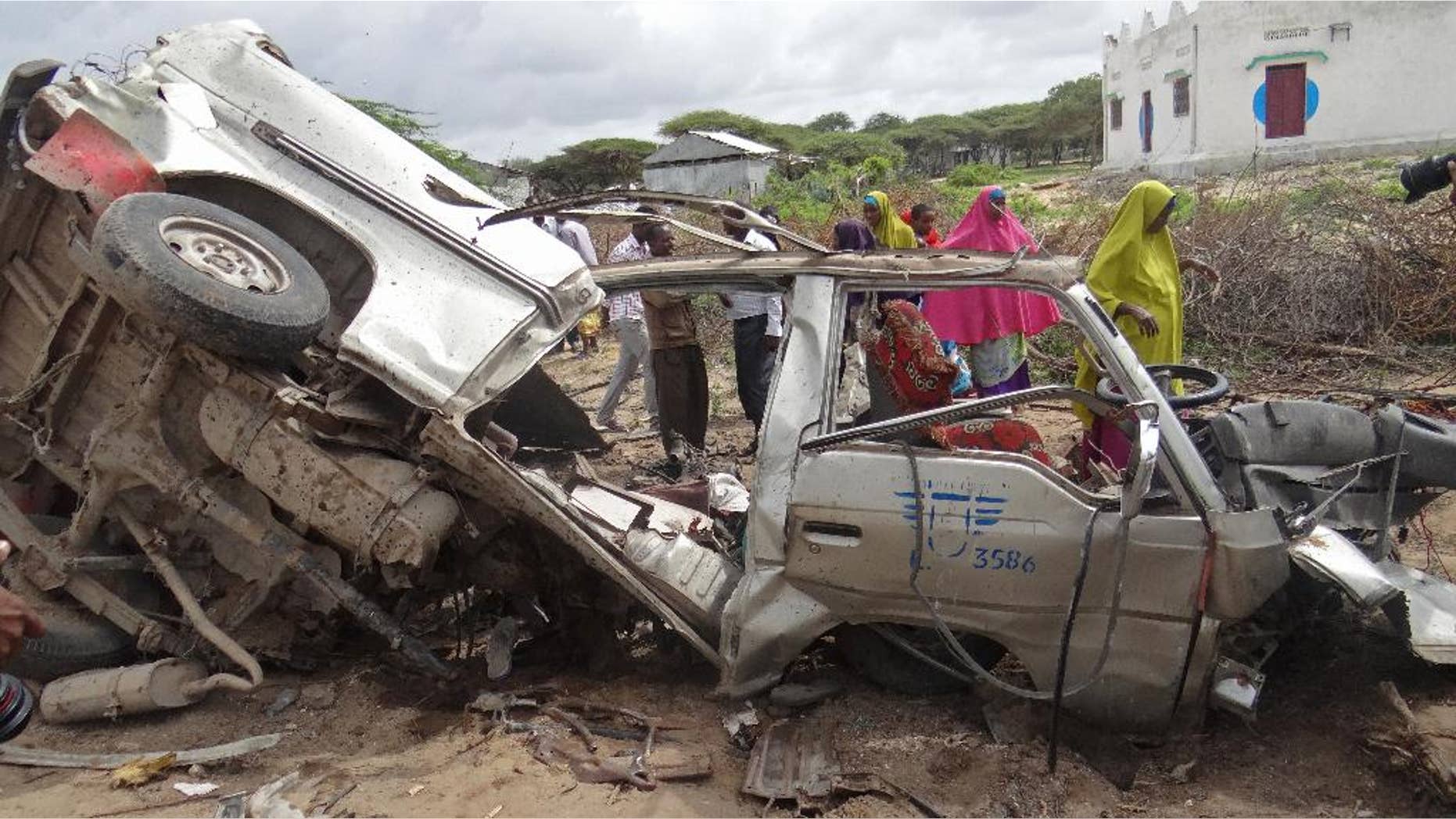 Somalis gather to look at a wrecked mini bus after it destroyed by a road side bomb at Lafoole outside Mogadishu, Somali. Thursday ,June,30,2016. A Somali police officer says a roadside bomb struck a minibus outside Somali capital, killing at a number of people. (AP Photo/Farah Abdi Warsameh)