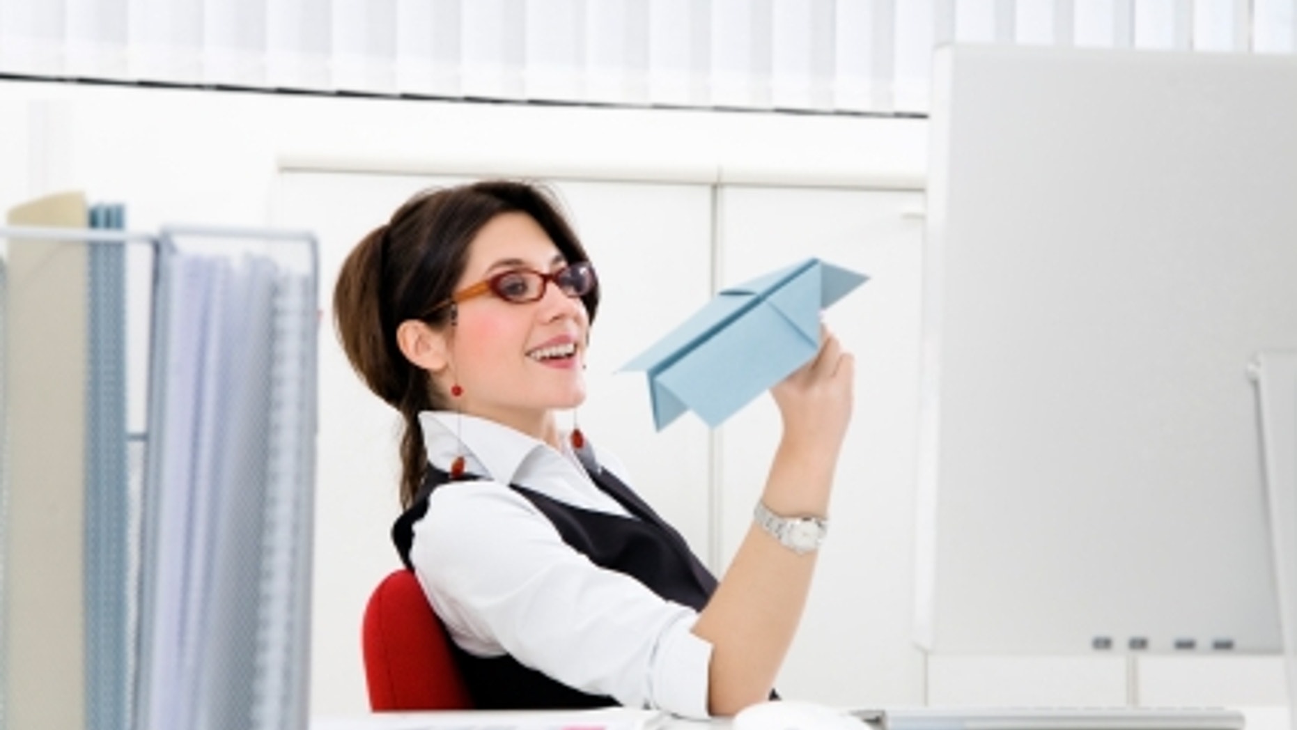 Young businesswoman throwing paper airplane in office