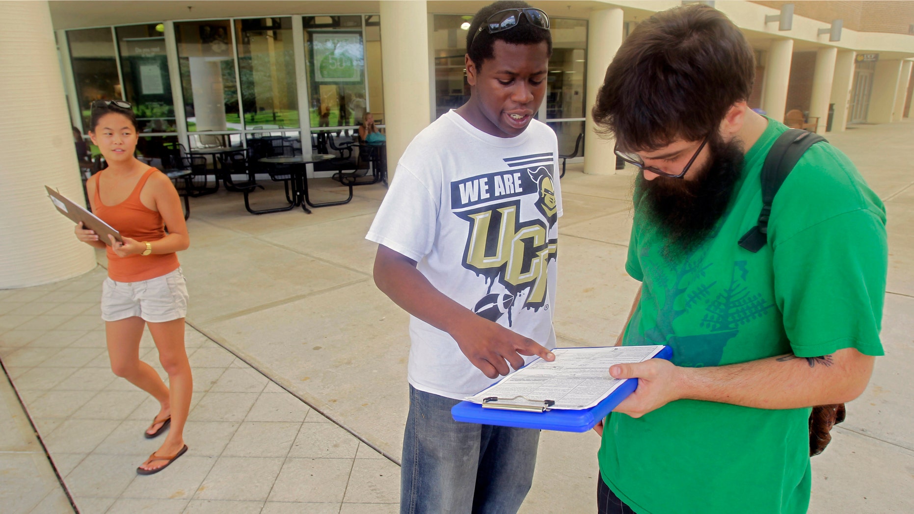 FILE: July 31, 2012: Aubrey Marks, left, watches Jordan Allen, center, as he helps student Casey Eirhstaedt, right, register to vote at the University of Central Florida in Orlando, Fla.